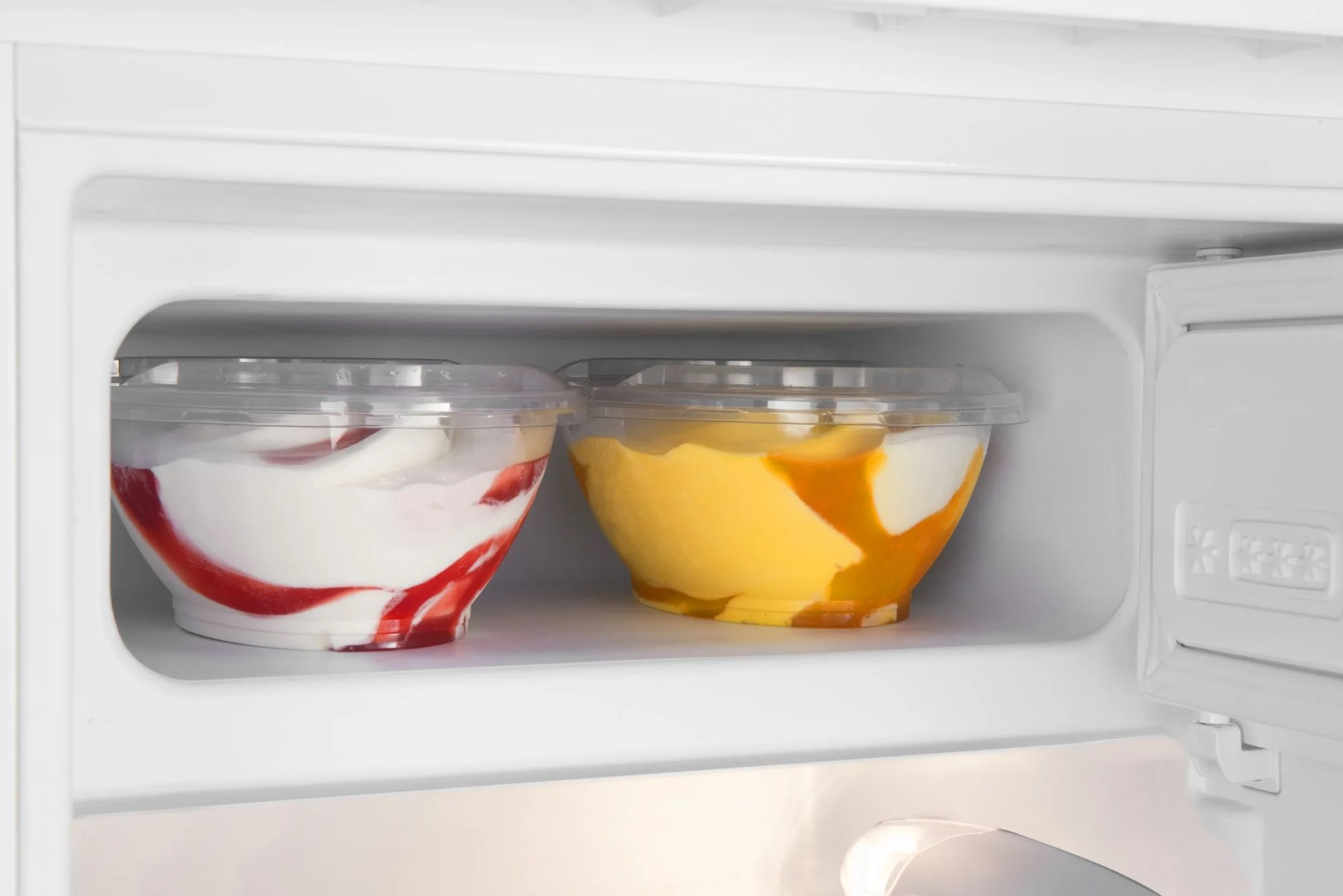 Dwa przezroczyste pojemniki z lodami, jeden czerwono-biały, jeden żółty, w lodówce.