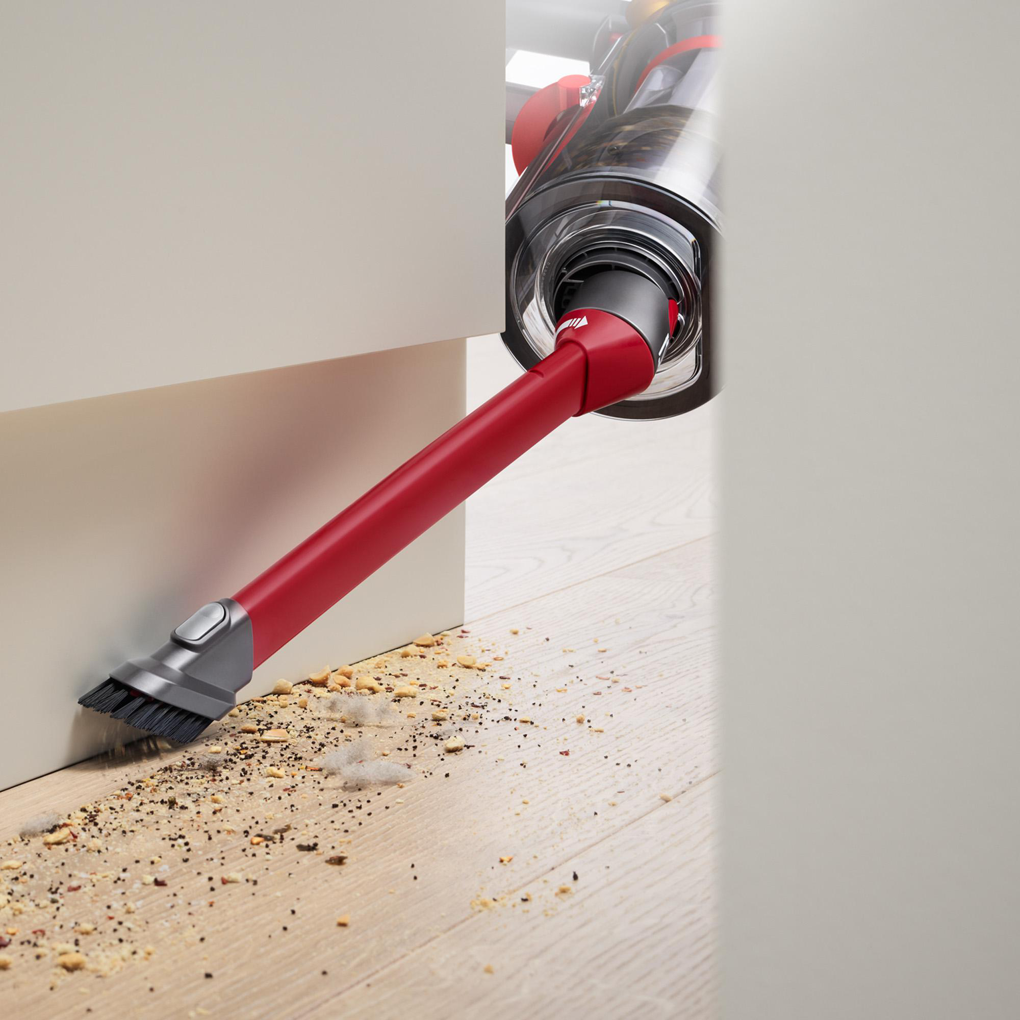 Eine rote Staubsaugerdüse reinigt einen Holzboden und entfernt Schmutz und Ablagerungen.