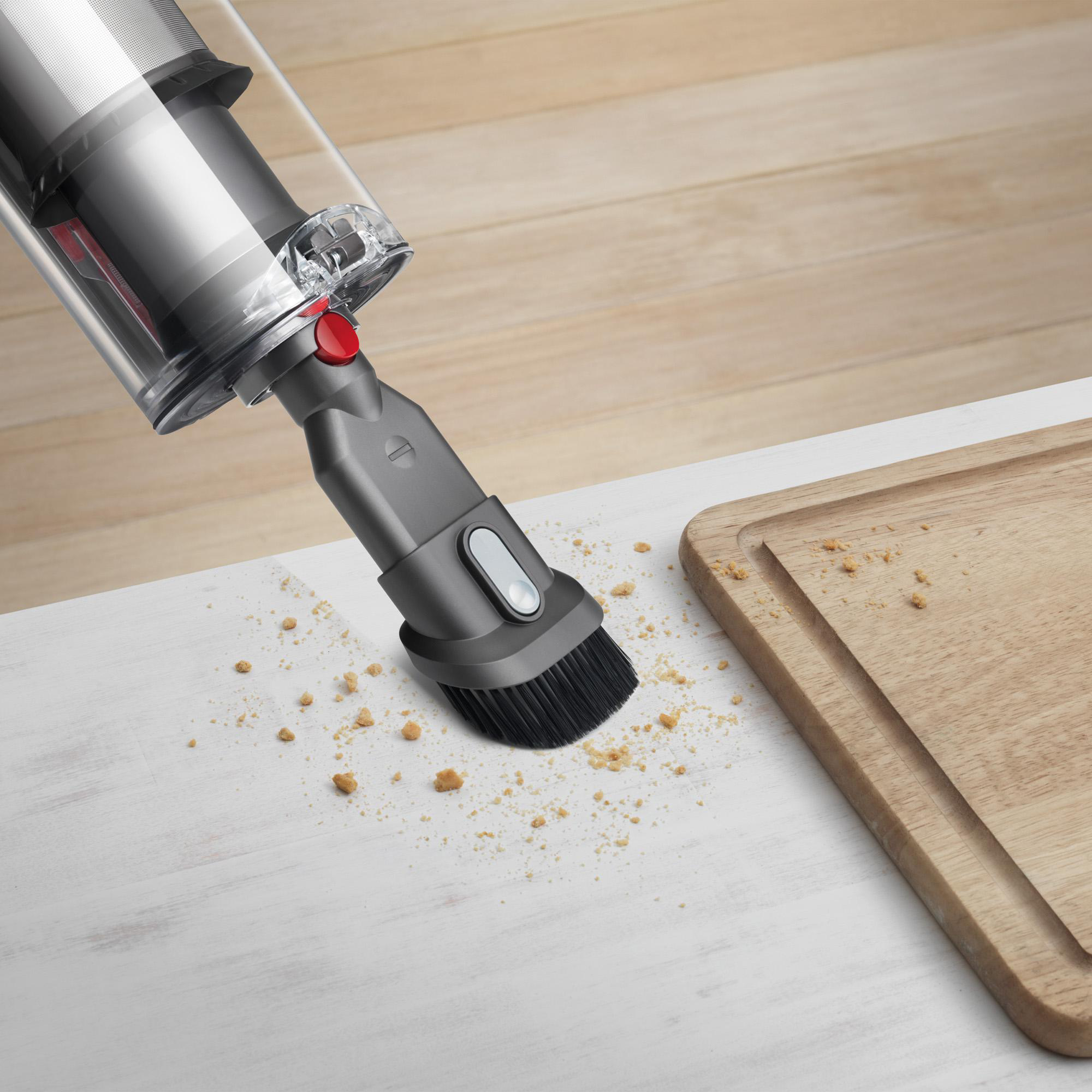 Staubsauger reinigt Krümel von weißer Oberfläche. Ein Holzschneidebrett ist daneben.