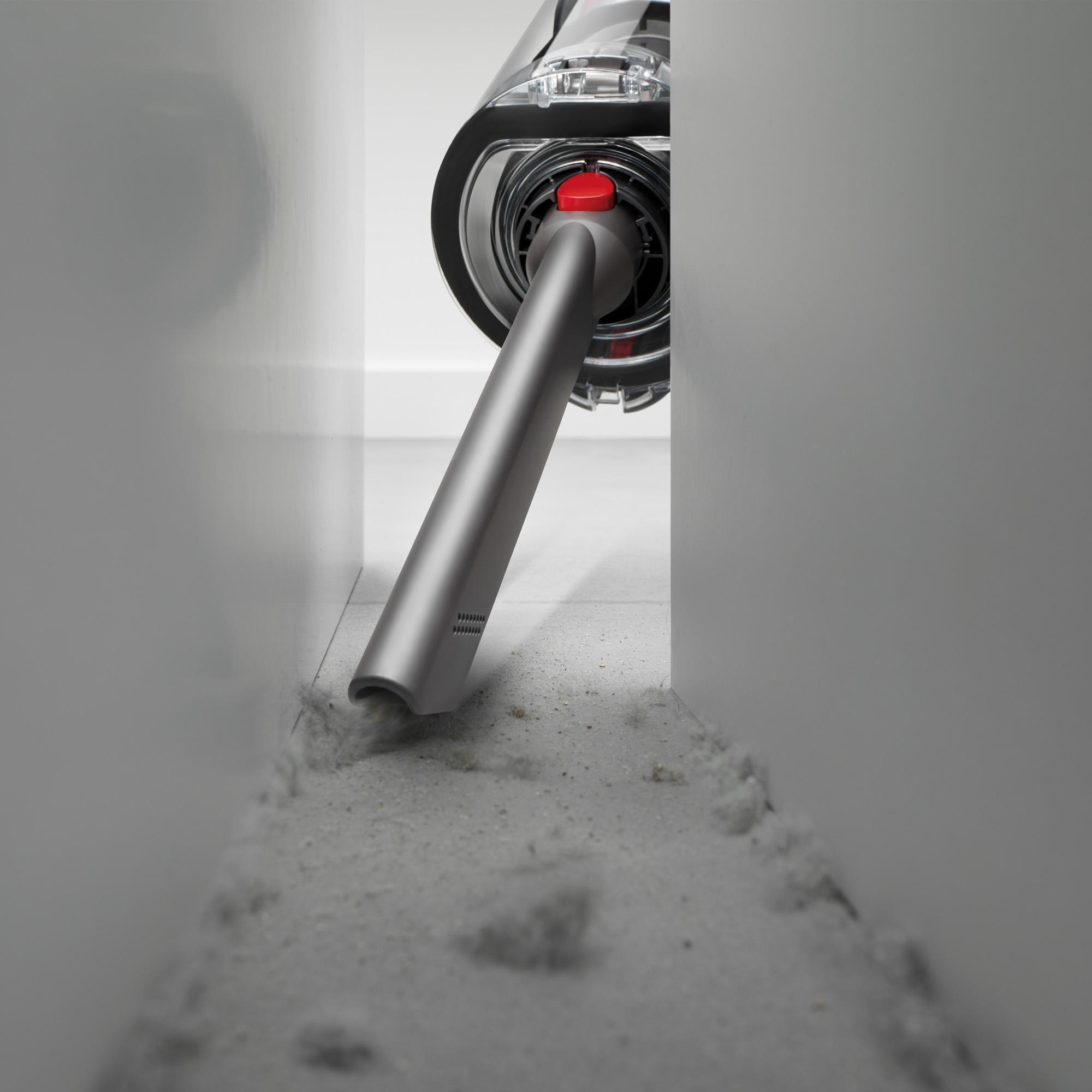 Dyson Staubsauger reinigt einen schmalen Raum. Grauer Staubsauger. Weiße Wände und Boden.