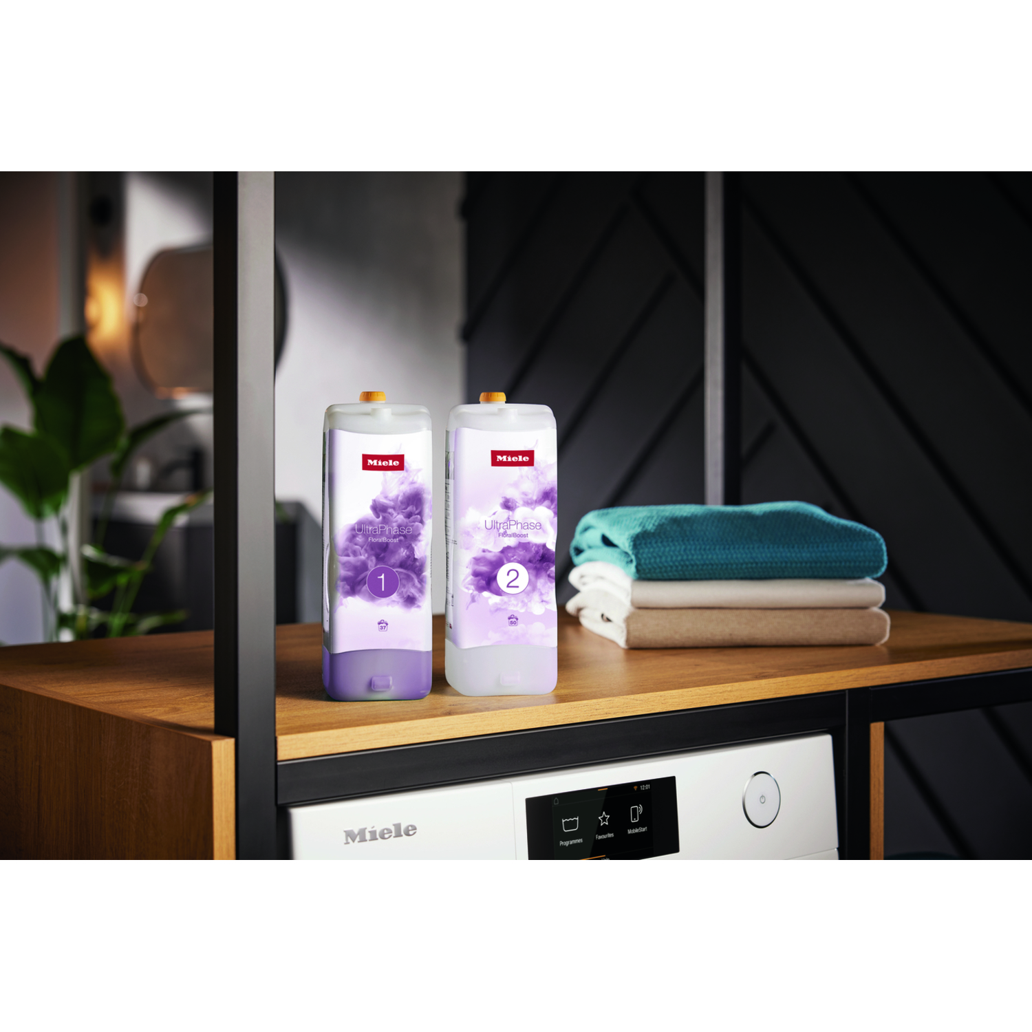Deux bouteilles de détergent sur une étagère, avec machine à laver et serviettes pliées en arrière-plan.