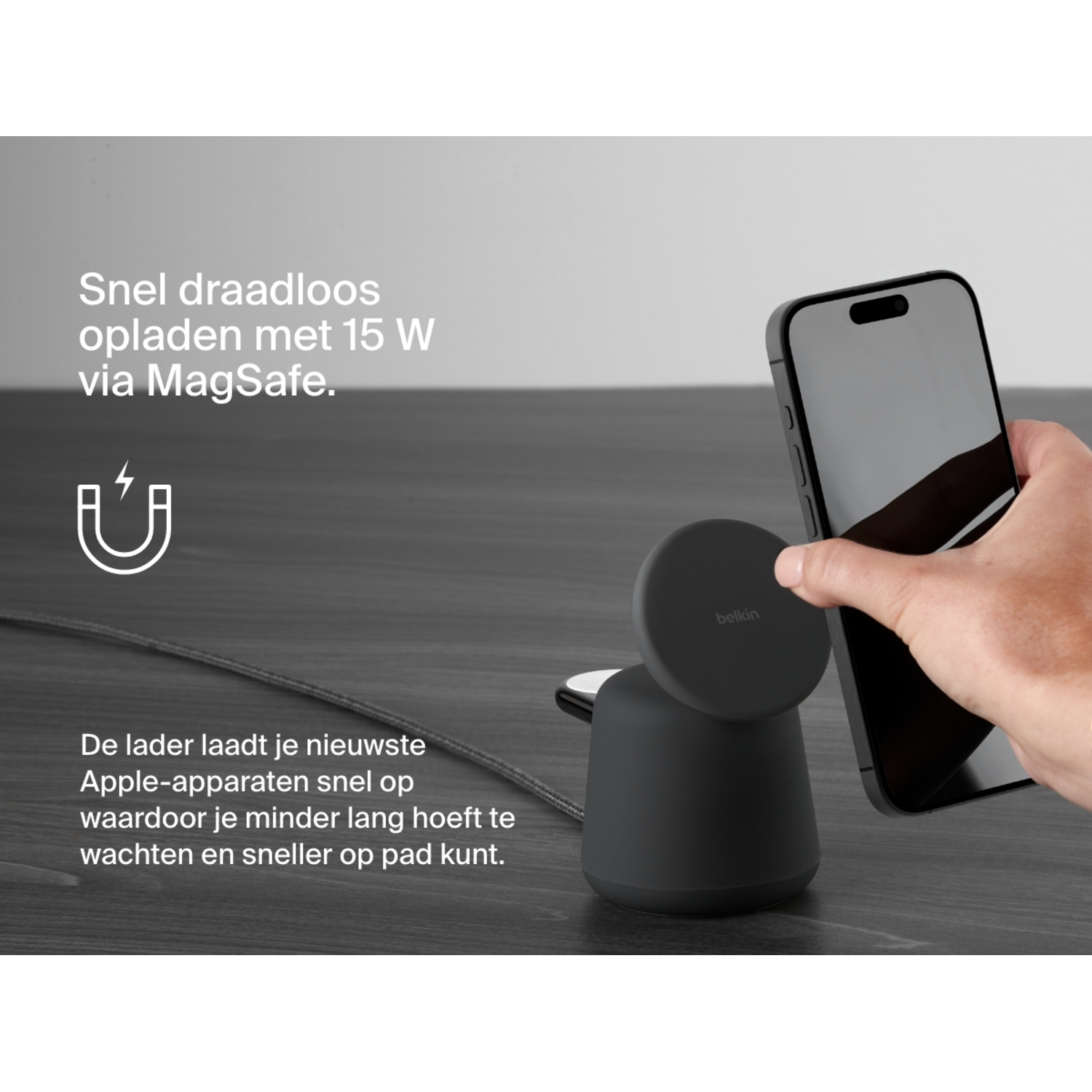 Persoon houdt een zwarte telefoon vast bij een zwarte draadloze oplader met tekst.