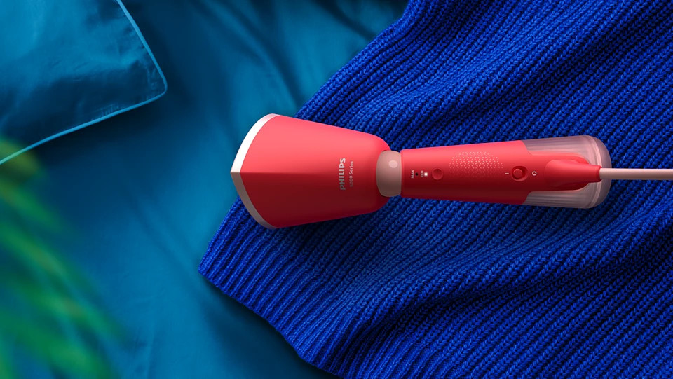 Czerwony parownik ręczny Philips na niebieskim kocu. Wydobywa się para.