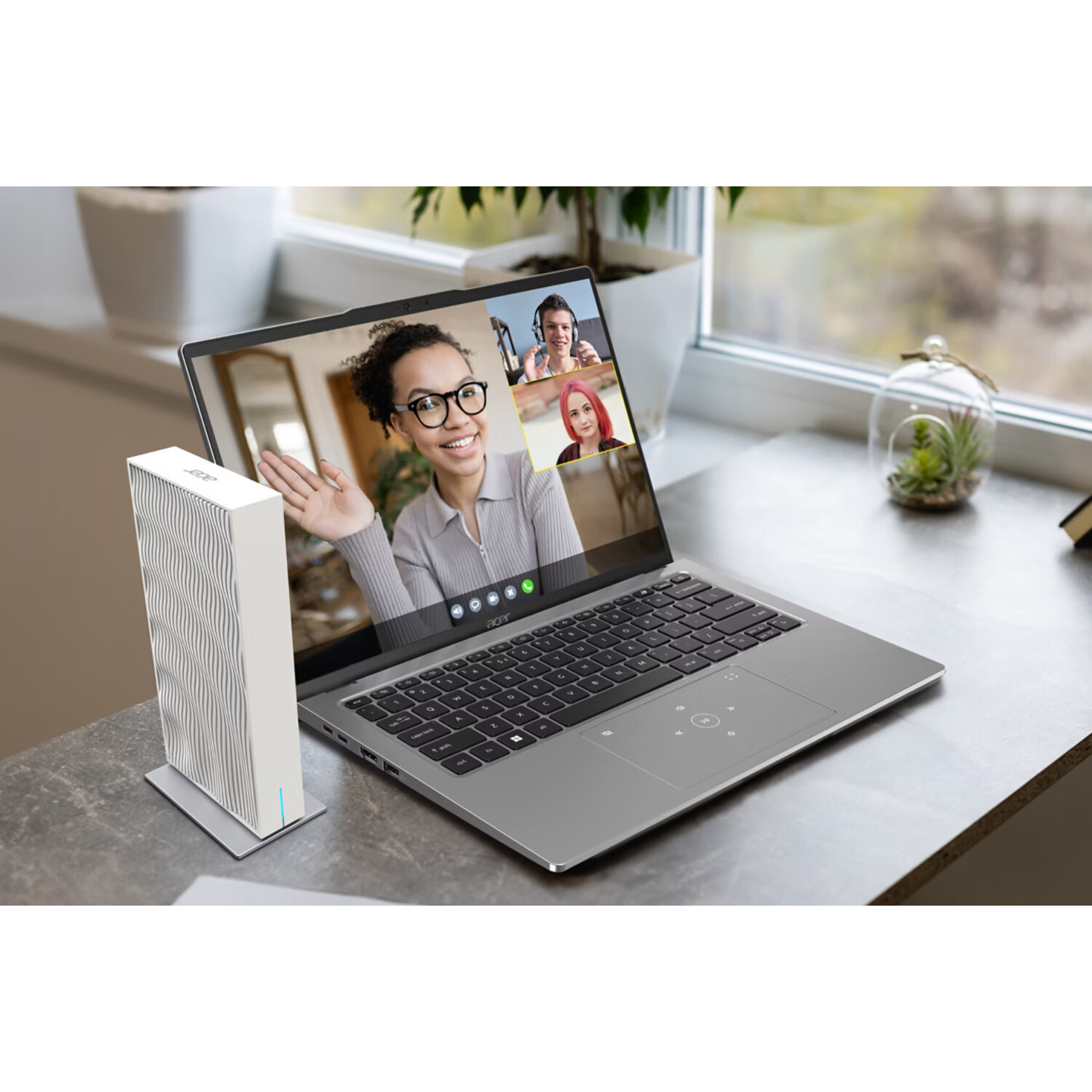 Laptop open op een bureau, videogesprek met drie deelnemers. Een witte luidspreker staat links.