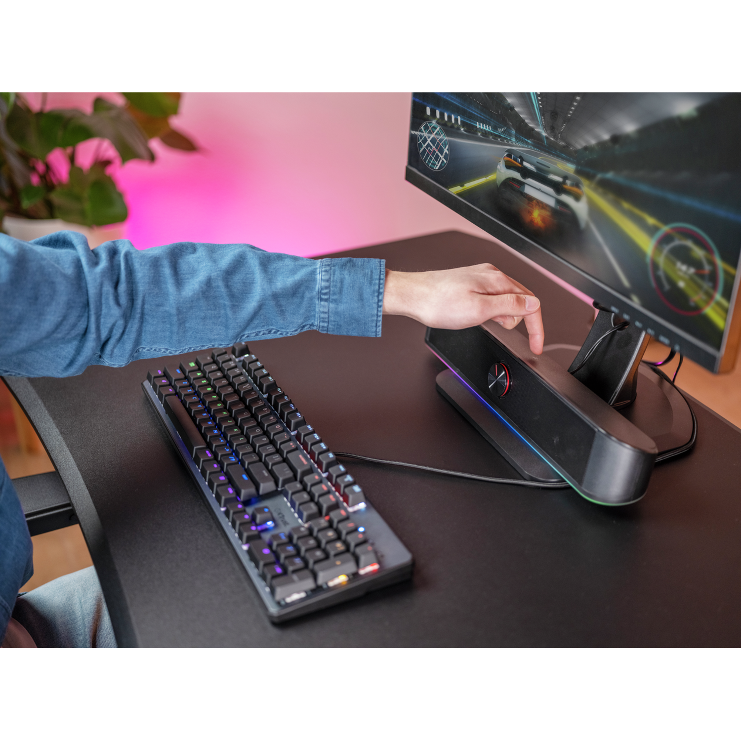 A person's hand interacting with a monitor and a keyboard, with a gaming device in between.