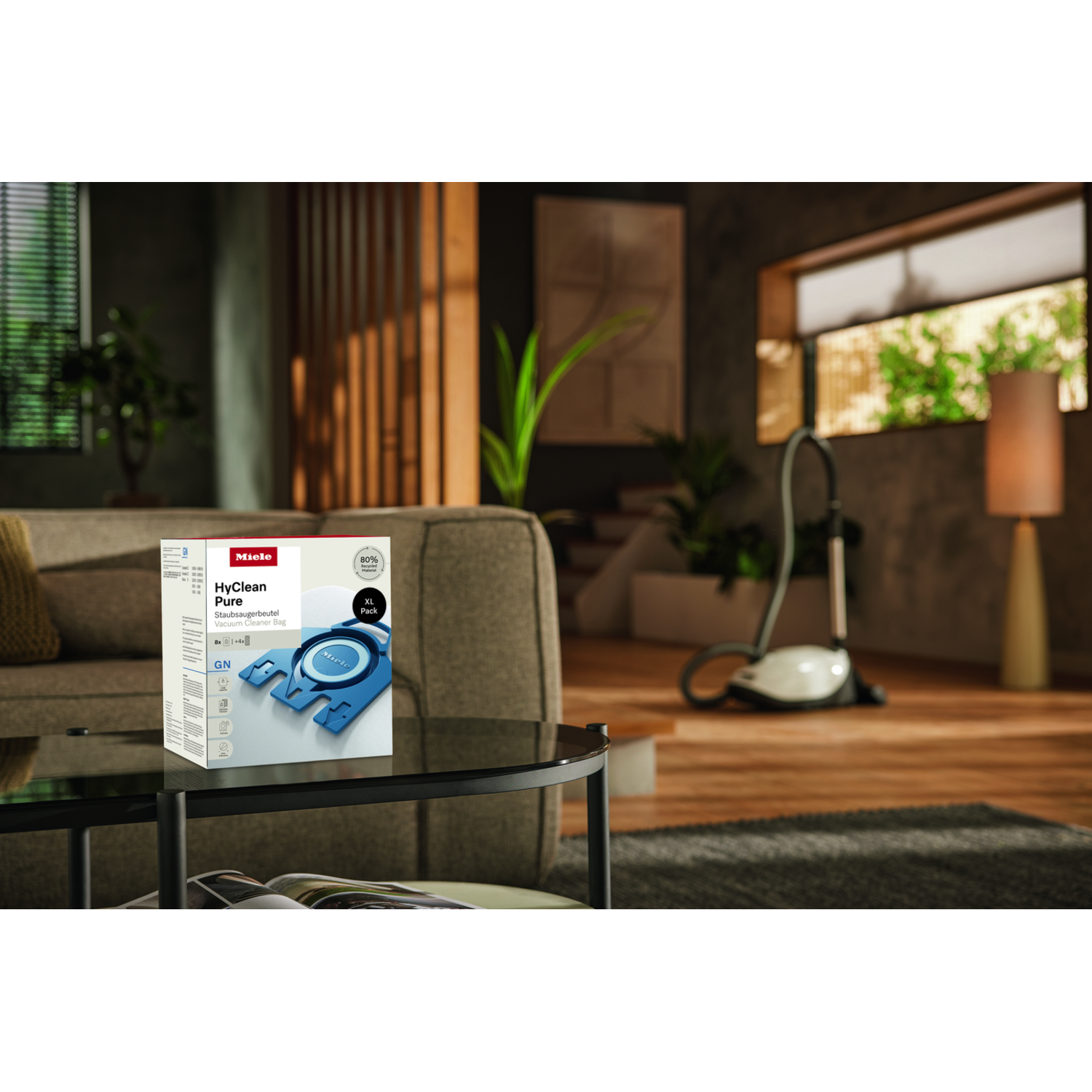 A living room features a sofa, a coffee table with a vacuum bag box, and a vacuum cleaner in the background.