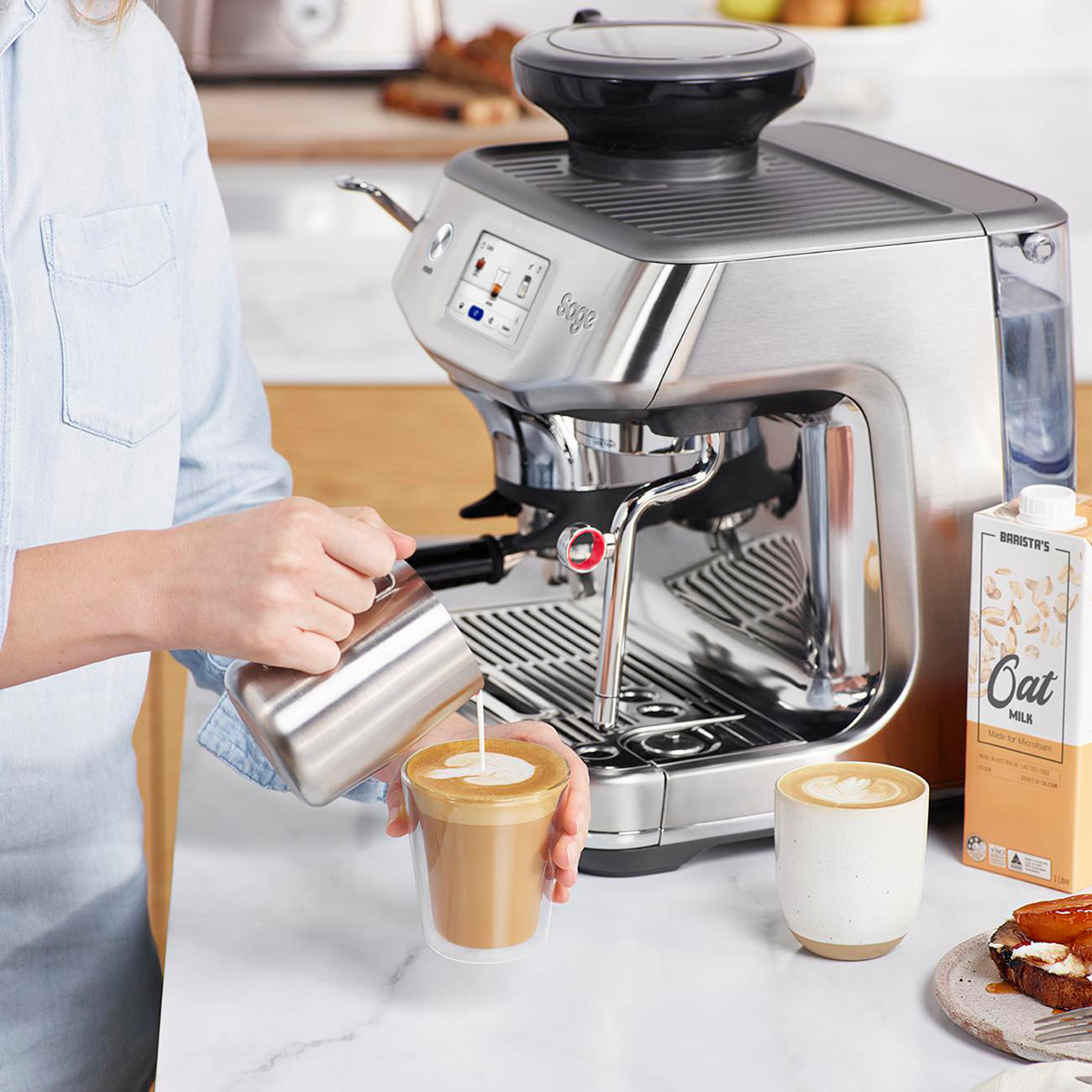 Person gießt Milch aus einem Karton in eine Tasse Kaffee. Kaffeemaschine ist sichtbar.
