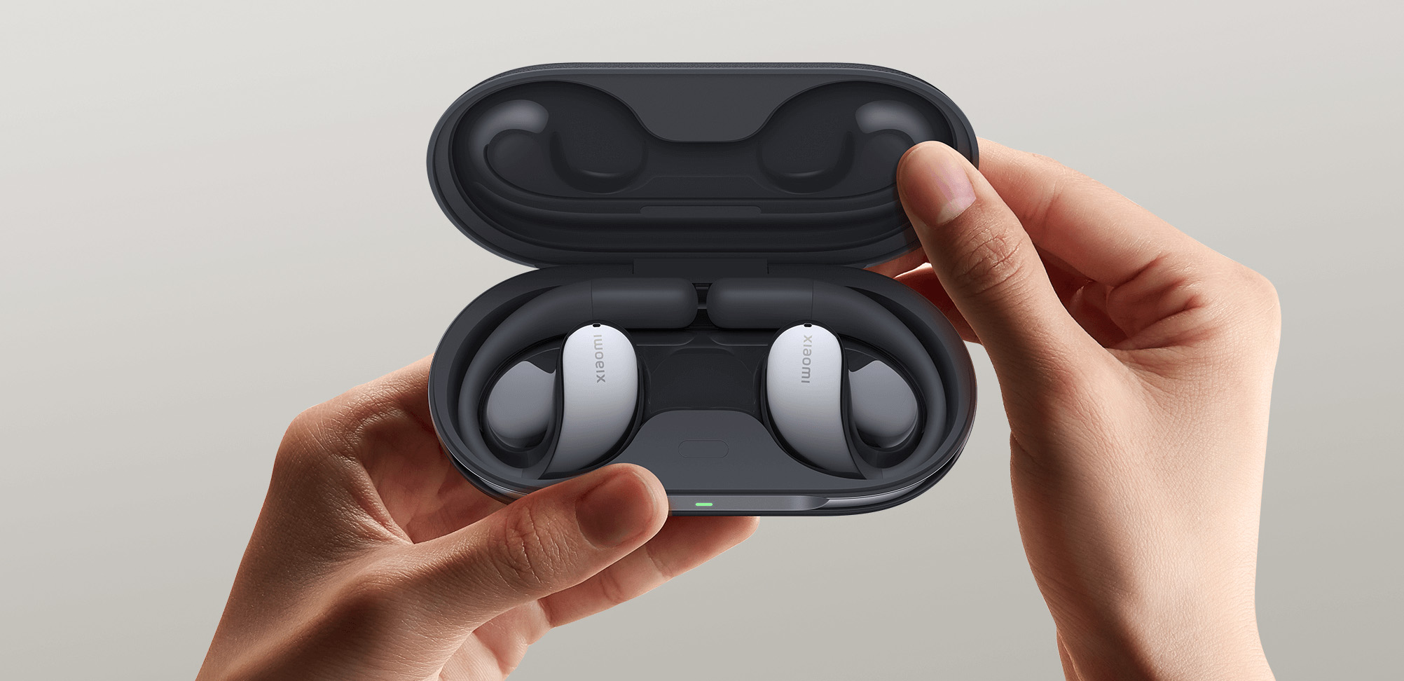 Dłonie otwierające czarne etui z białymi słuchawkami Xiaomi w środku. Szare tło.