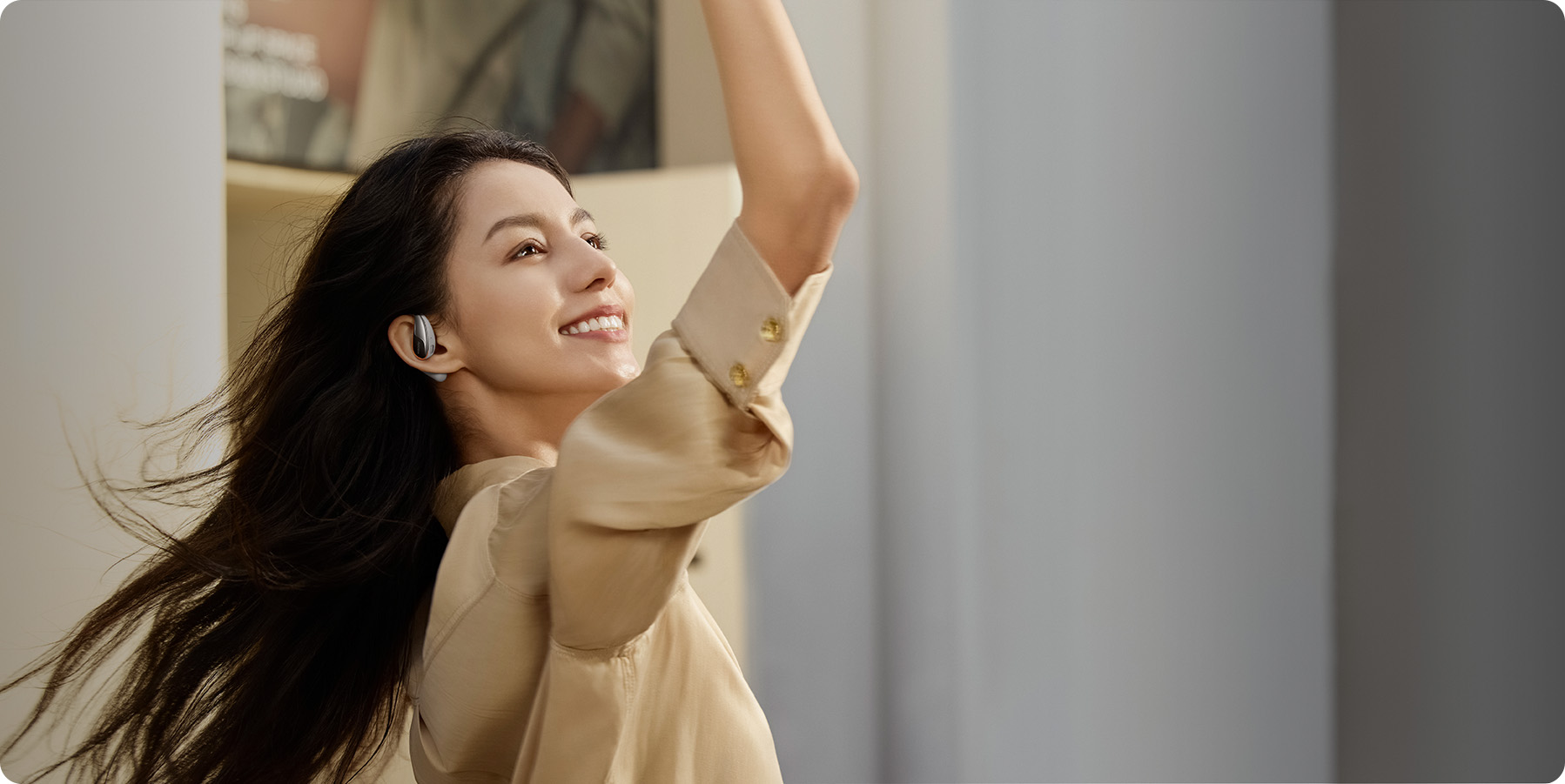 Kobieta ze słuchawkami, uśmiechnięta i podnosząca ramię. Białe tło.