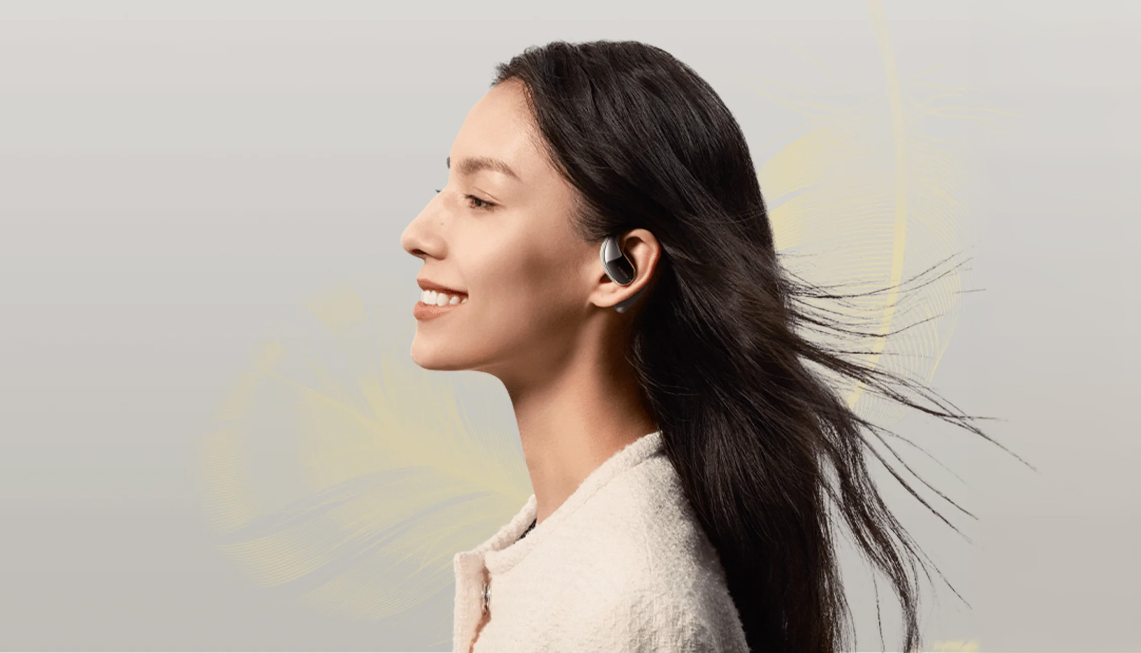 Kobieta z czarnymi włosami uśmiechnięta, z wkładką douszną. Żółty, przypominający pióra wzór w tle.