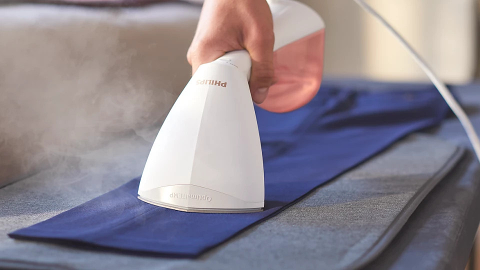 Osoba używa białego i różowego parowacza Philips do niebieskich spodni.