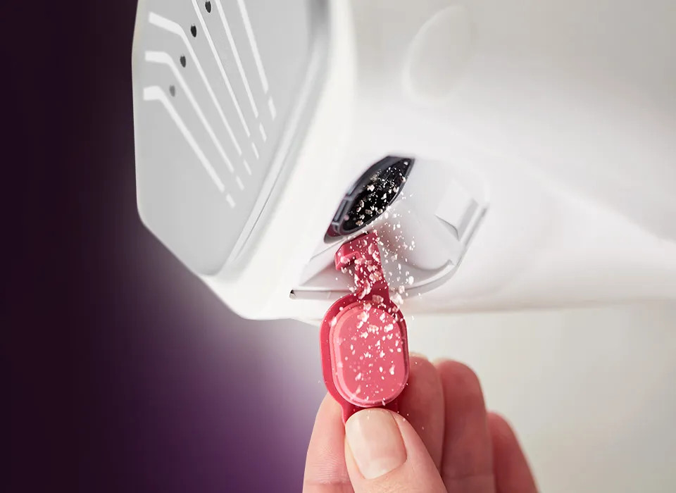 Ręka dozująca detergent do dozownika pralki, z rozmytym tłem.