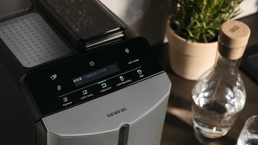 Kávéfőző digitális kijelzővel, amely a cappuccino opciót mutatja. Egyéb gombok: eszpresszó és tej.