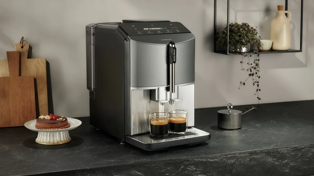 Espresszó gép két csésze kávéval. Ezüst és fekete design. Torta a tányéron, dekoráció és sötét munkalap.