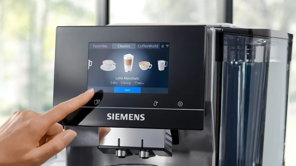 Kávéfőző érintőképernyője, egy ujj a Latte Macchiato opcióra mutat.