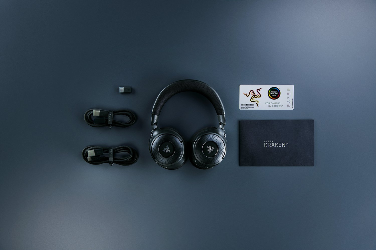 Cuffie Razer nere, cavi, dongle e scheda su superficie grigia. Scatola Kraken presente.