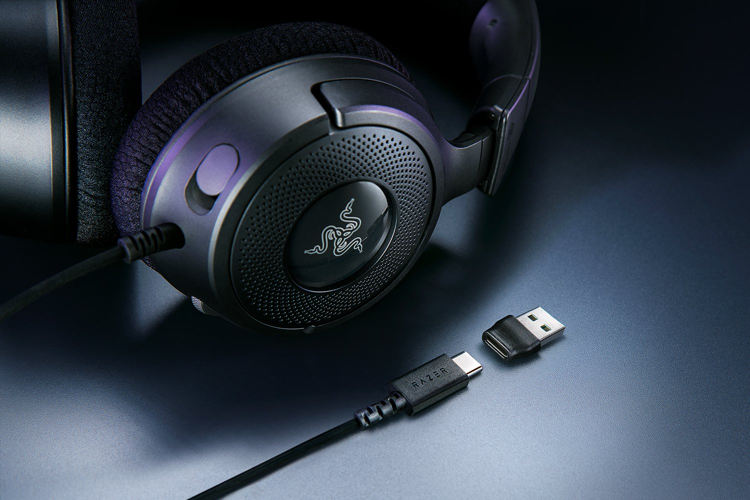 Cuffie Razer nere con cavo e adattatore da USB-C a USB-A su superficie scura.