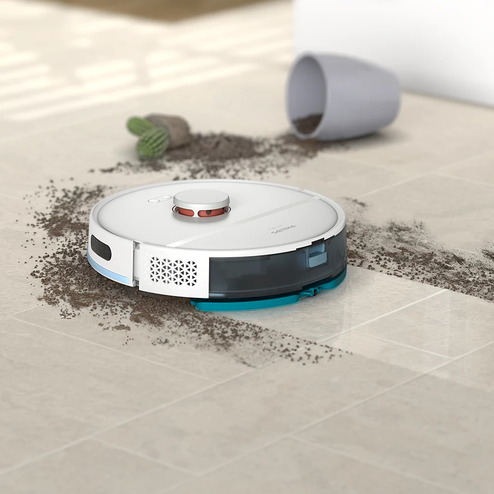 Robot sprzątający na podłodze wyłożonej płytkami z brudem i upadłą rośliną.
