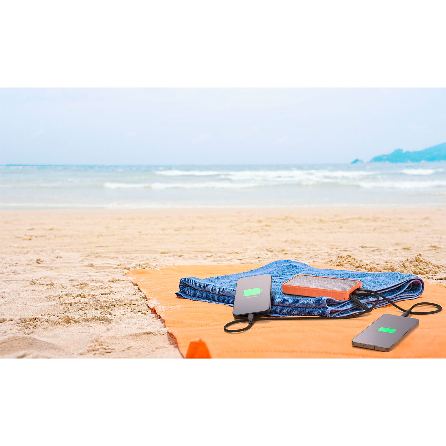 Scena sulla spiaggia con un asciugamano arancione, dispositivi in carica e un asciugamano blu.