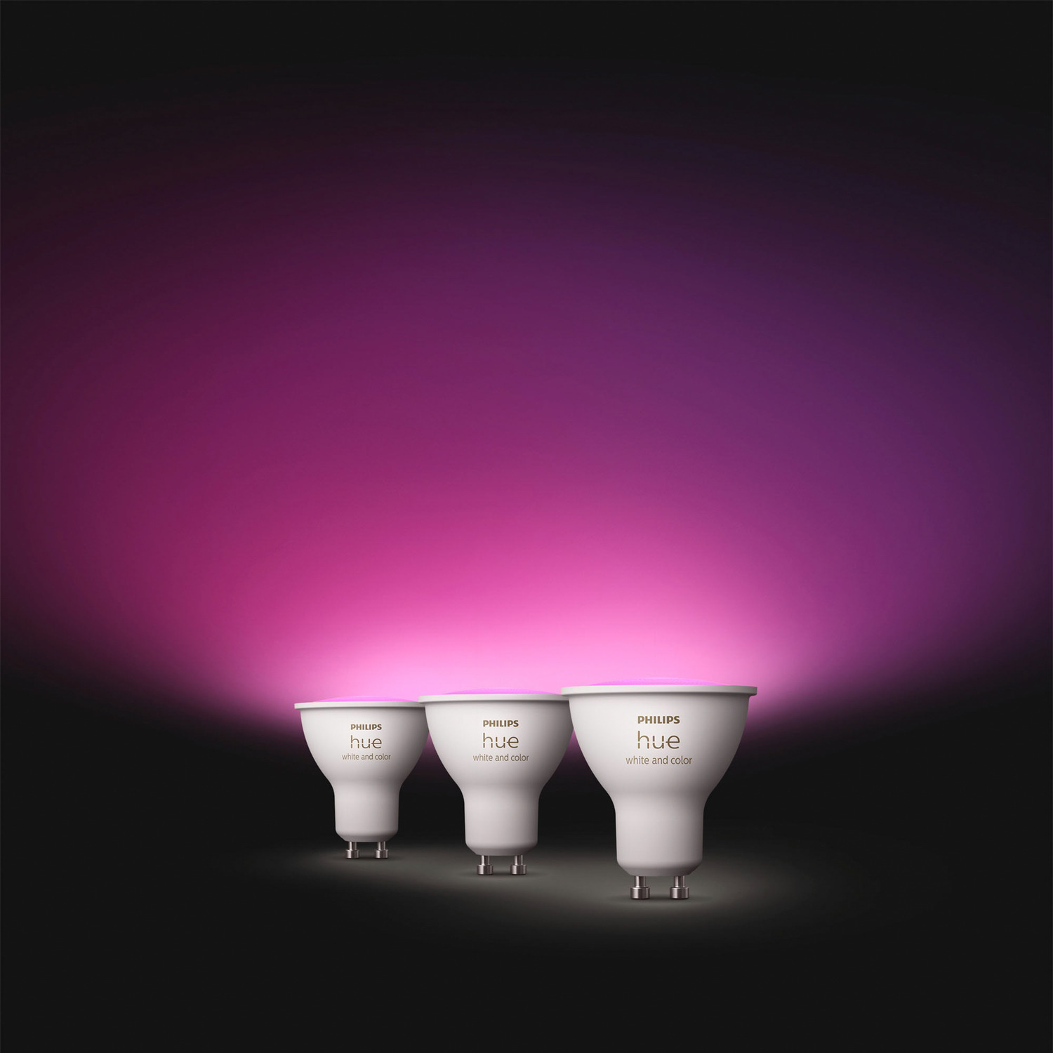 Trois ampoules intelligentes Philips Hue blanches, brillant en rose et violet. Fond noir.