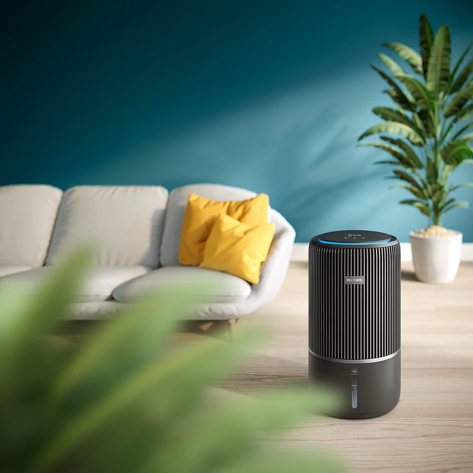 Nowoczesny salon z sofą, żółtymi poduszkami, rośliną i oczyszczaczem powietrza na drewnianej podłodze.