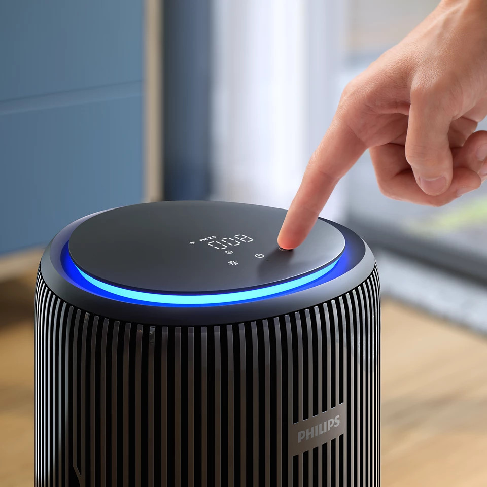 Dłoń dotykająca oczyszczacza powietrza Philips z niebieskim światłem. Wyświetlacz cyfrowy. Schemat kolorów czarno-szary.