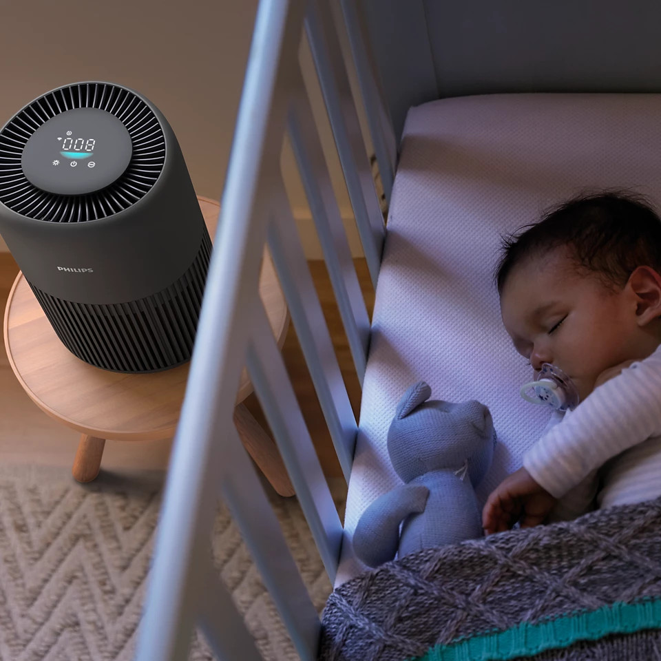 Dziecko śpiące w kołysce z oczyszczaczem powietrza na pobliskim stoliku.