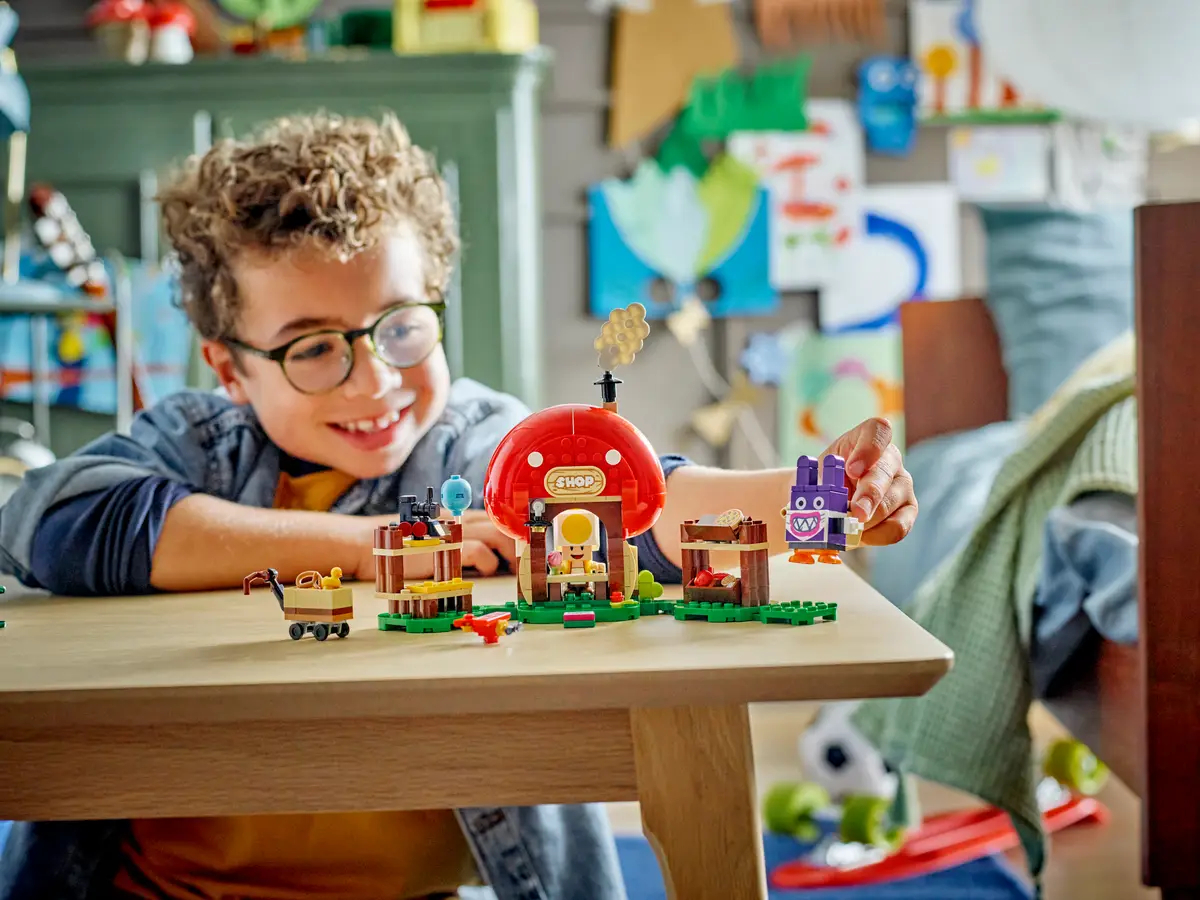 Chłopiec bawiący się zestawem LEGO. Uśmiecha się, a zestaw stoi na drewnianym stole.