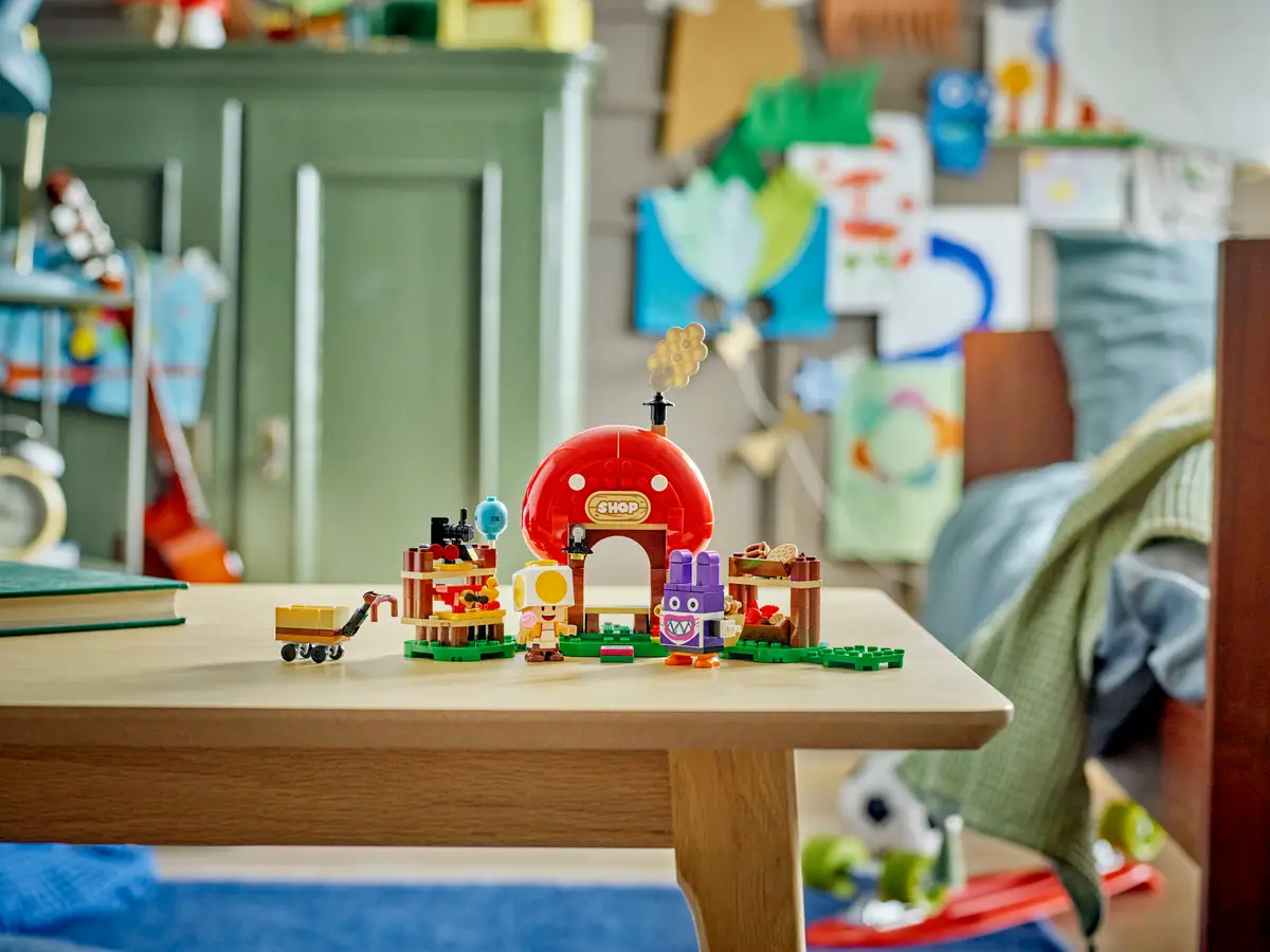 Zestaw LEGO z czerwonym domkiem grzybowym i postaciami. Drewniany stół w pokoju.