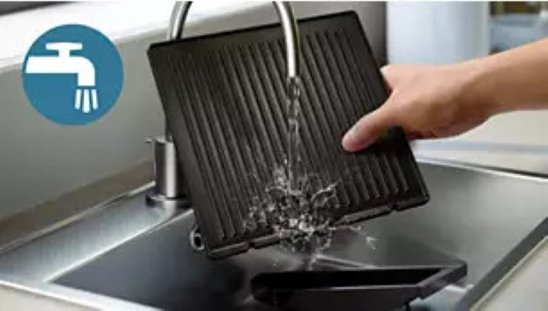 Osoba czyści płytę grilla pod bieżącą wodą w zlewie.