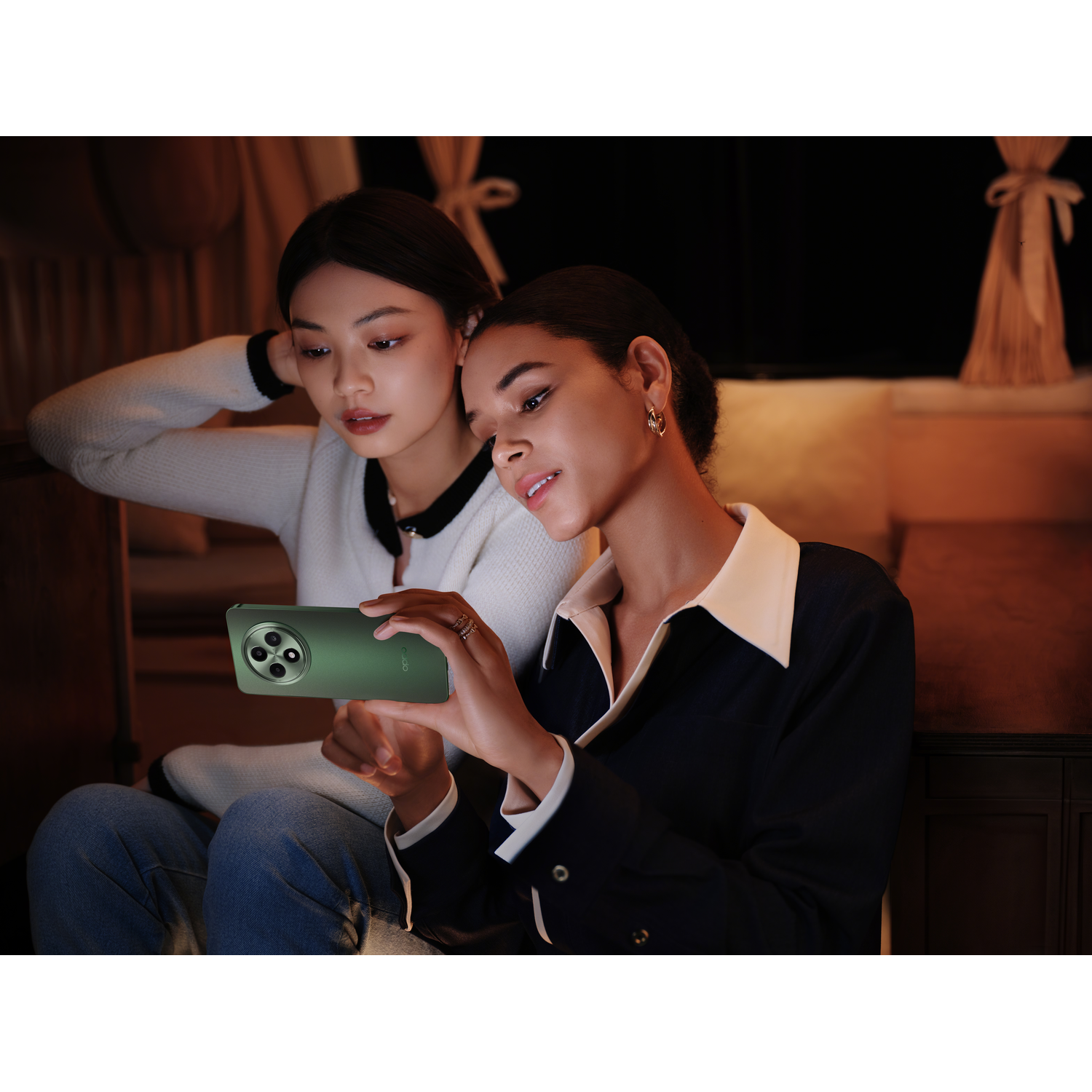 Two women looking at a green smartphone, with a cozy setting.