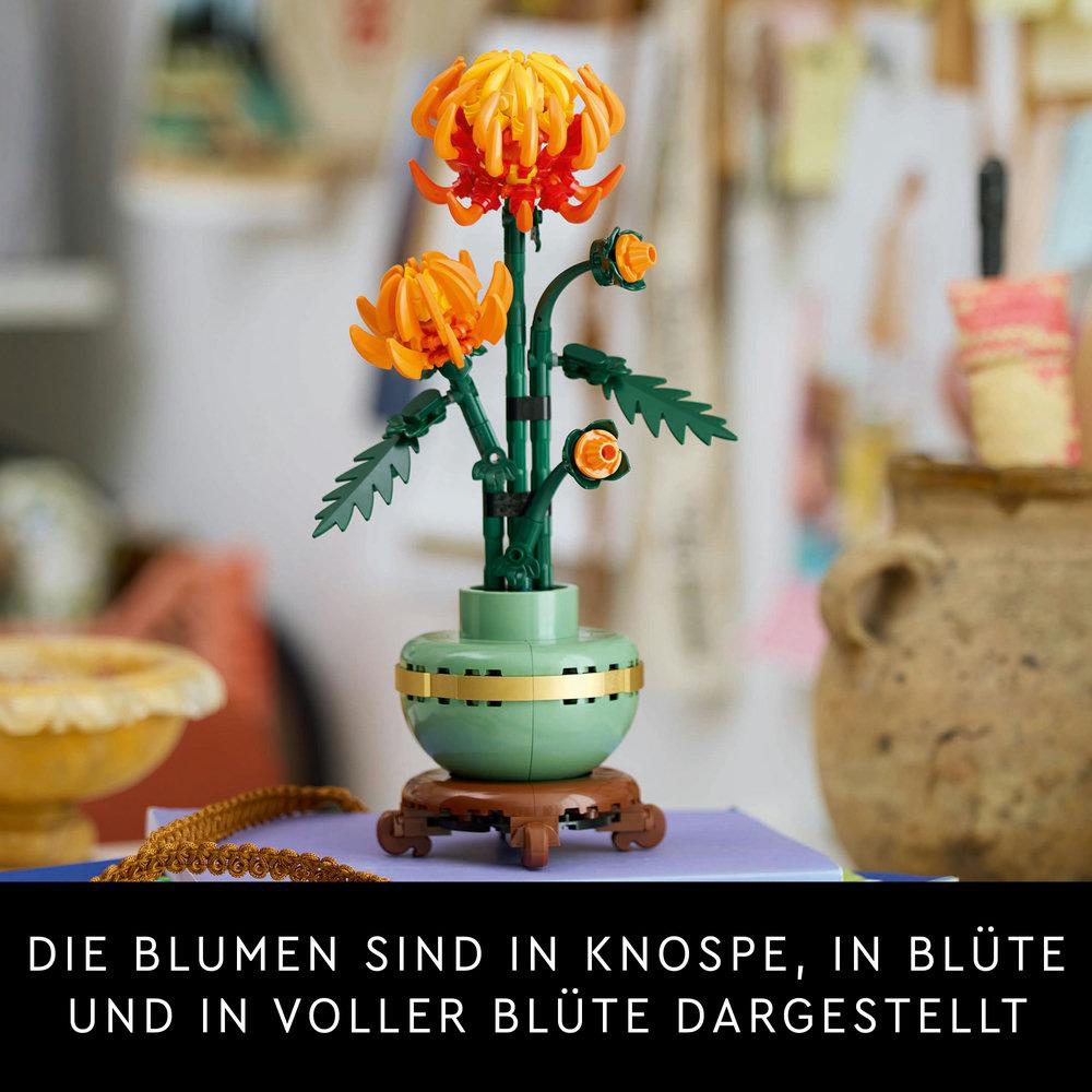 Ein LEGO Blumenset in einer Vase. Orange und grüne Blumen stehen auf einem Holzständer auf lila Oberfläche.