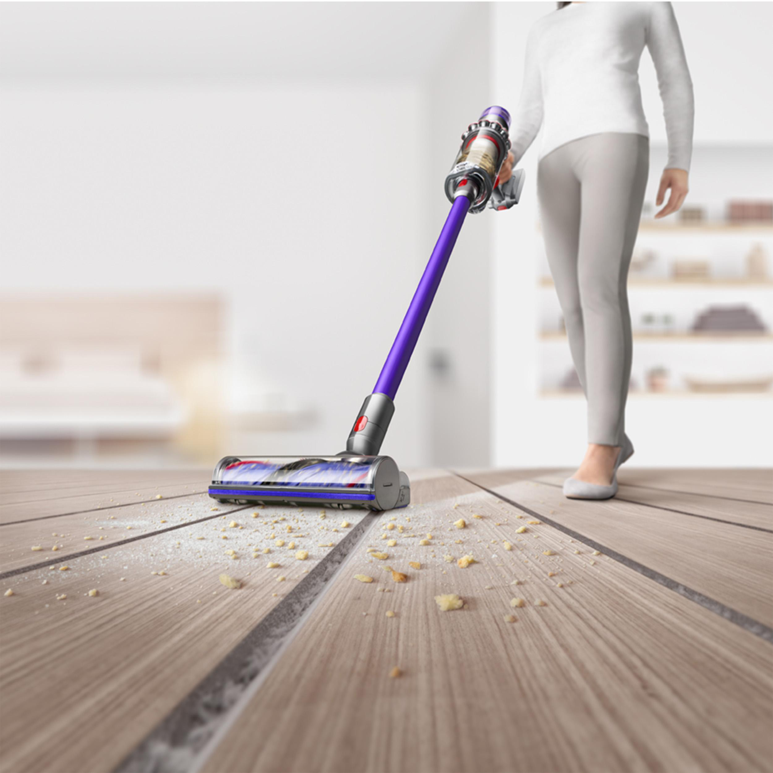 Person saugt einen Holzboden mit einem lila-grauen Staubsauger. Staub und Schmutz sichtbar.