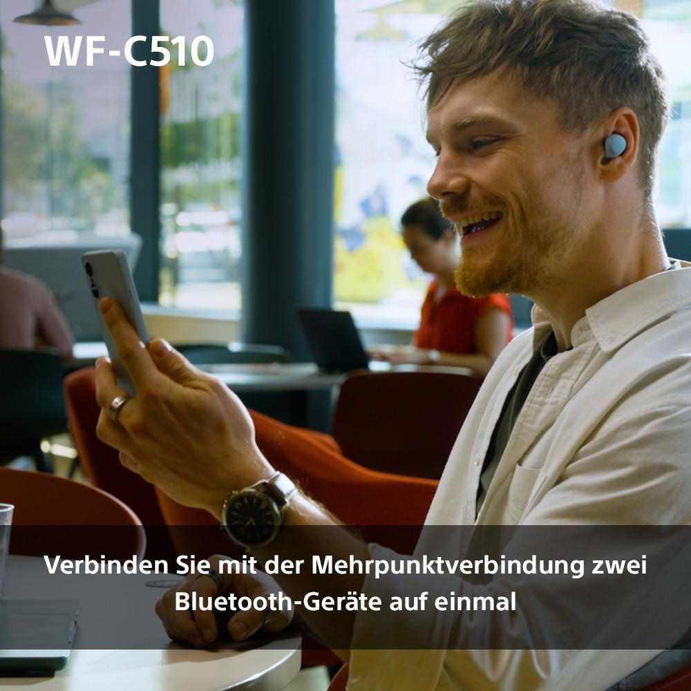 Ein Mann mit Ohrhörern und Handy, eine weitere Person im Hintergrund.