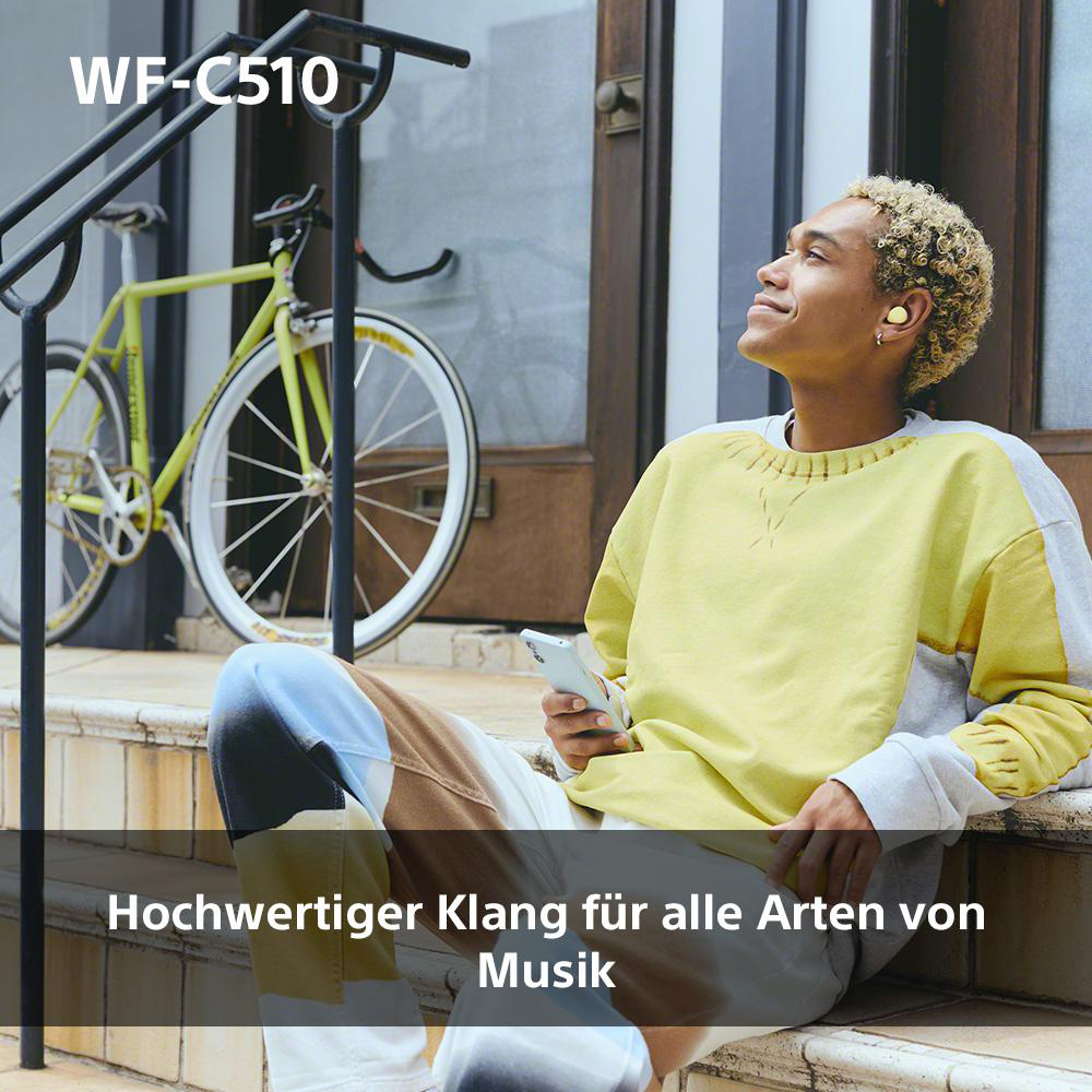 Mann mit gelbem Hemd und Ohrhörern sitzt auf Stufen neben Fahrrad.
