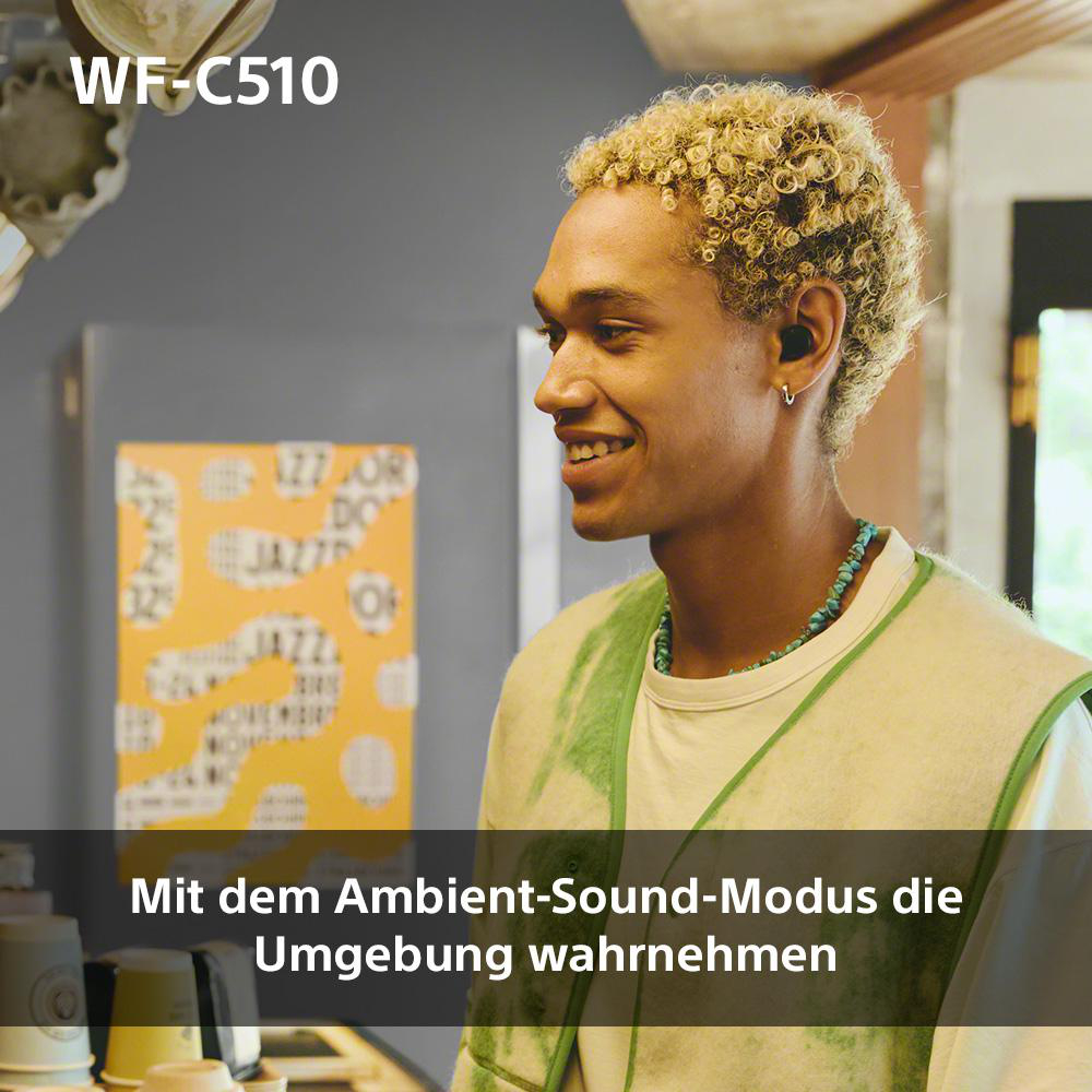 Ein Mann mit lockigem Haar, Kopfhörern und grüner Jacke, lächelt in die Kamera.