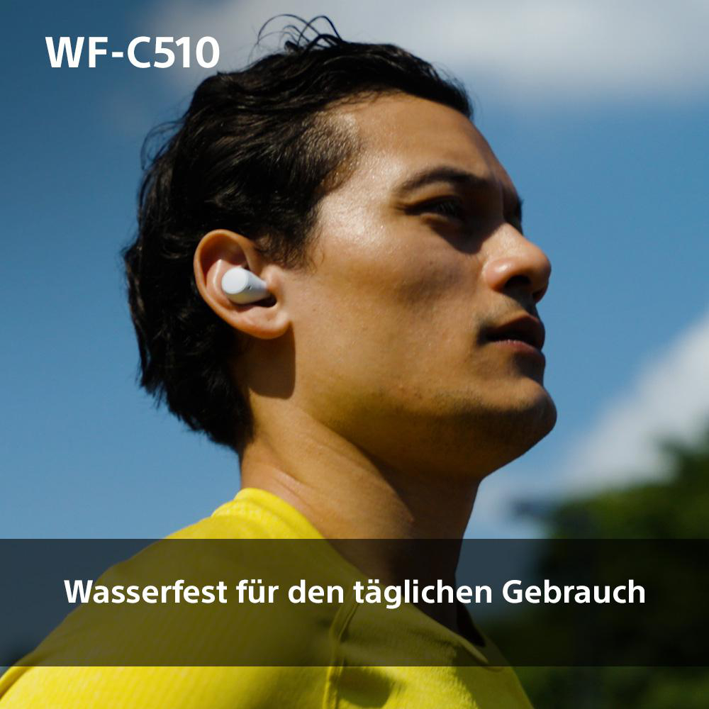 Ein Mann mit Ohrhörern, der vor blauem Himmel nach oben schaut.