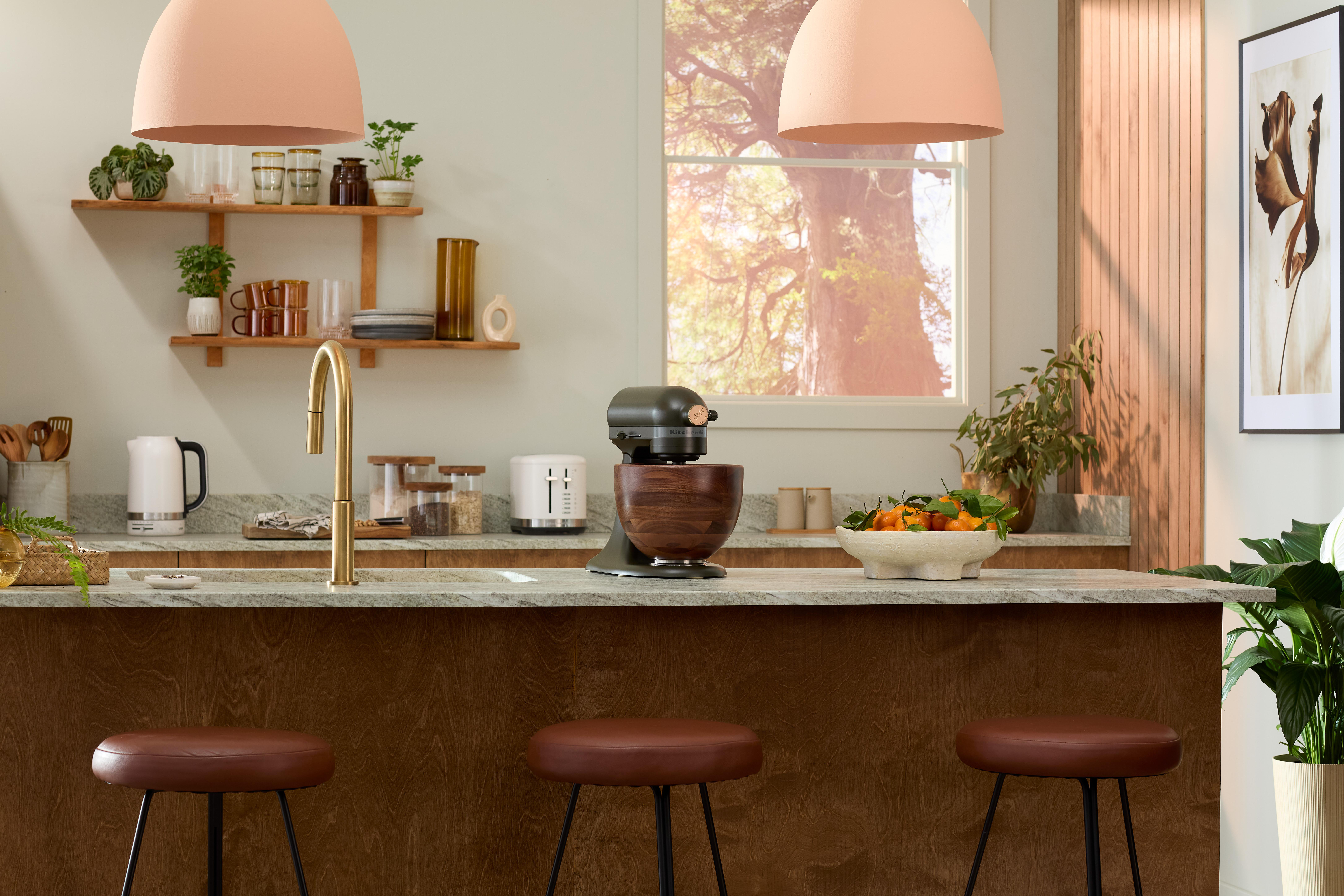 Moderne Küche mit Holzinse, Hockern und Mixer. Deckenlampen und Regale sind sichtbar.
