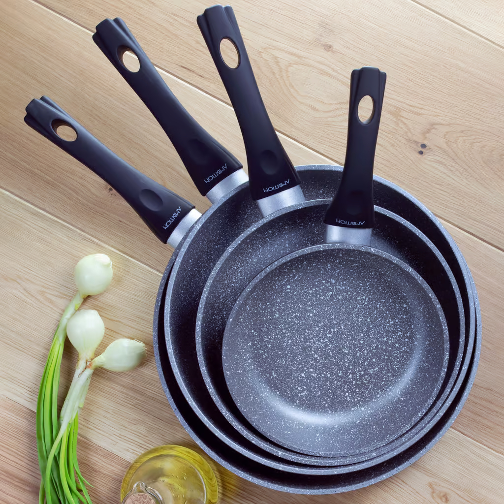 Zestaw patelni, z czarnymi uchwytami, na drewnianej powierzchni.