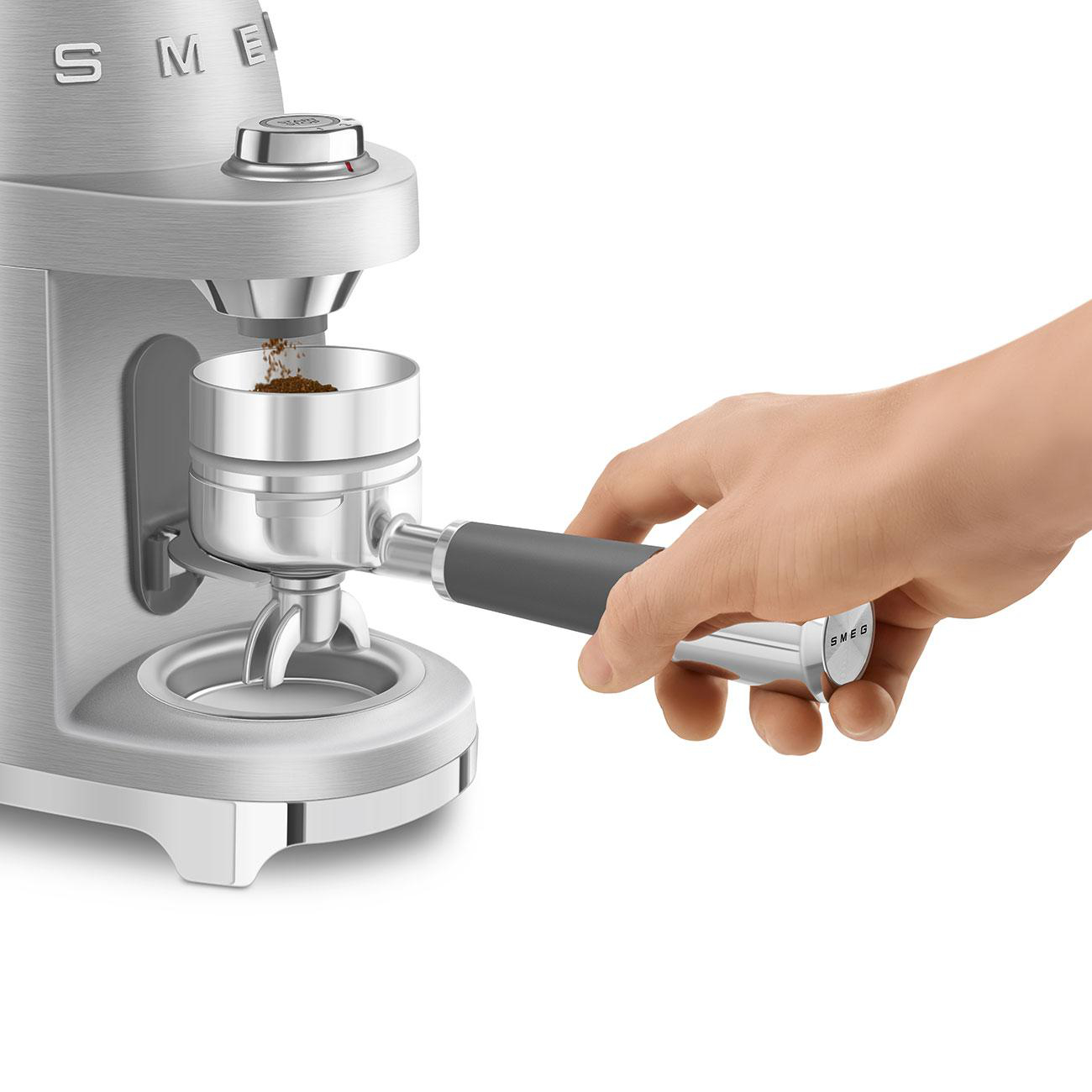 Eine Hand, die einen Siebträger mit gemahlenem Kaffee befüllt, mit einer Kaffeemühle.