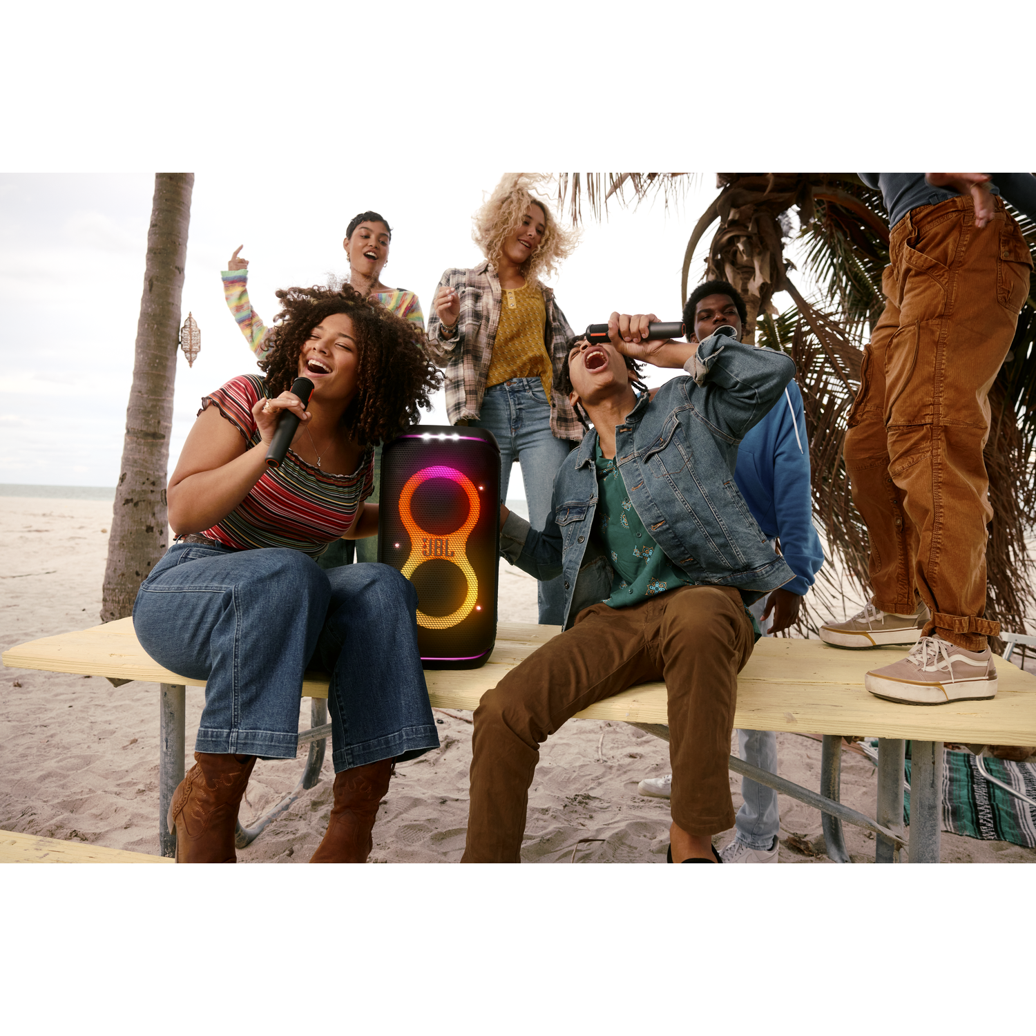 Group of people singing into microphones, with a JBL speaker.