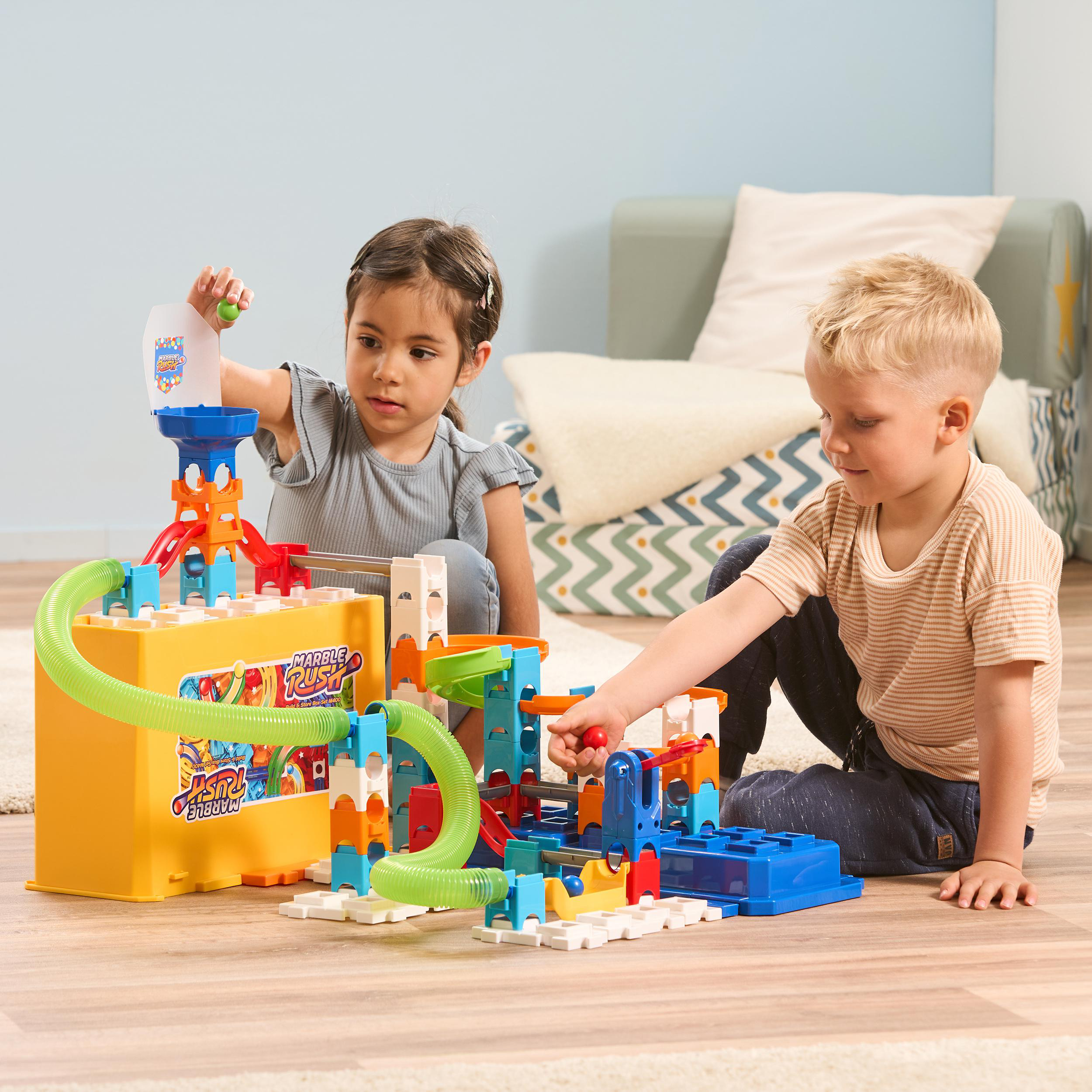Zwei Kinder spielen mit einem bunten Murmelbahnspielzeug. Einer gießt Murmeln ein, der andere justiert eine Bahn.