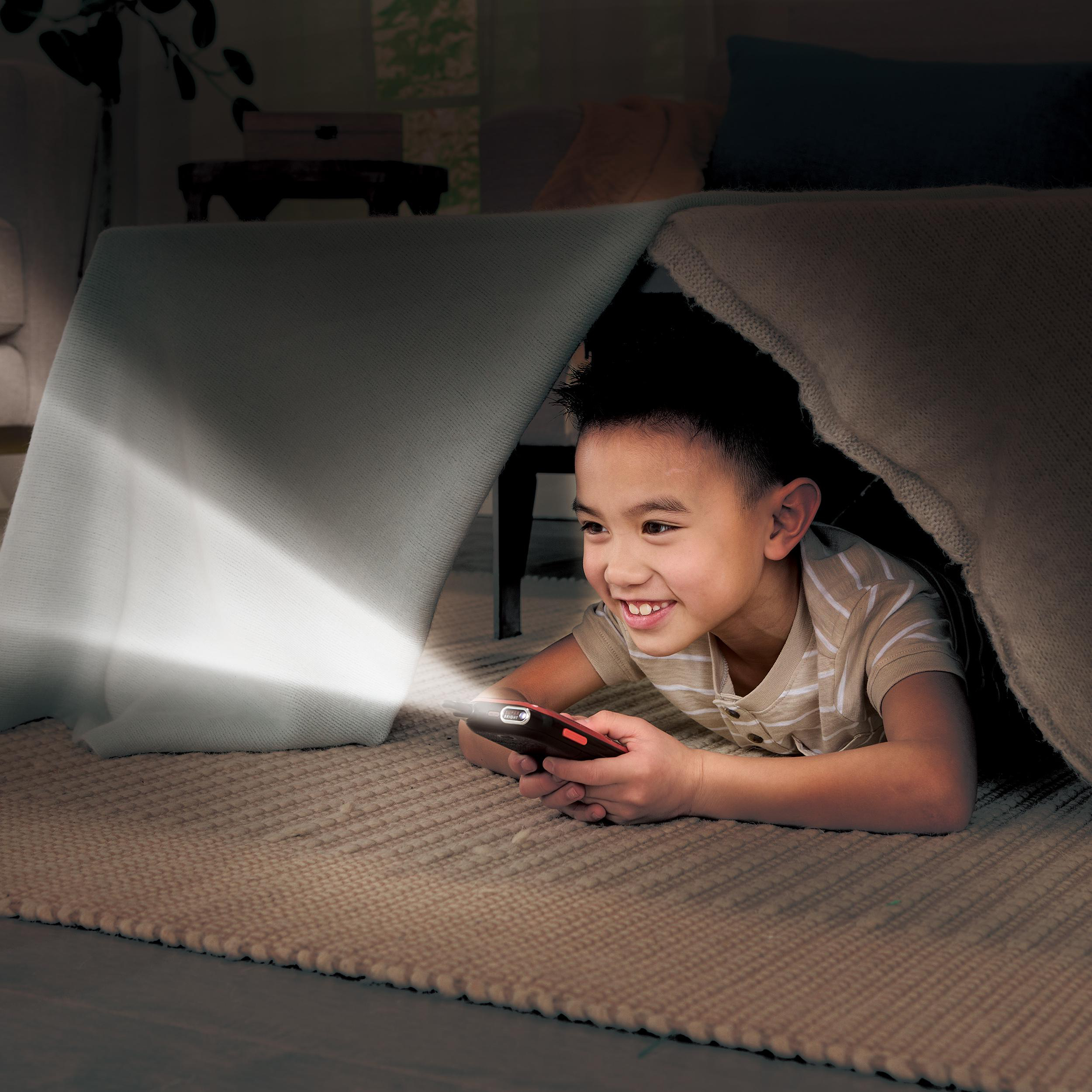 Ein Junge liegt in einer Deckenfestung, lächelt und hält ein Telefon, auf das ein Licht scheint.