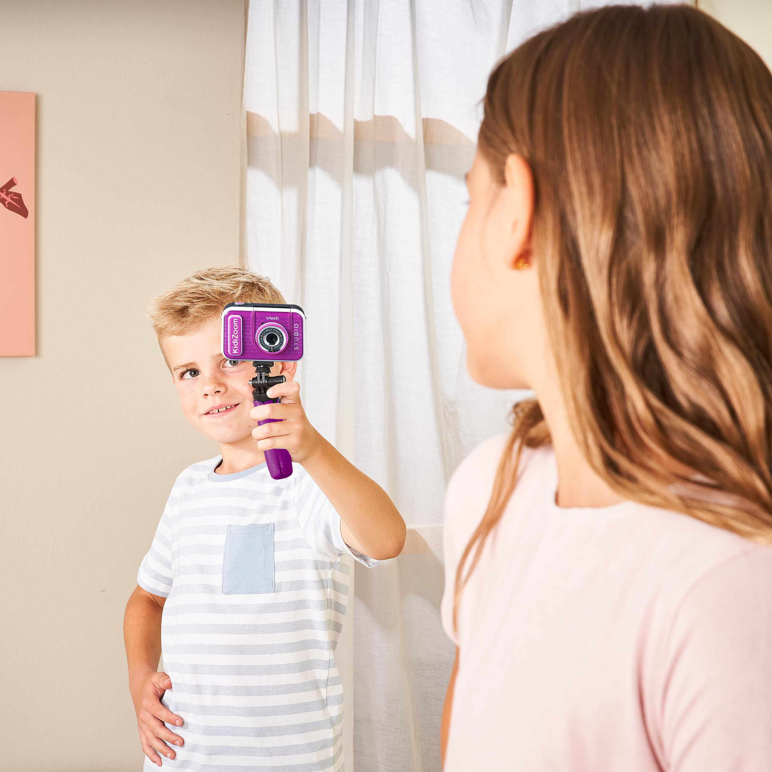 Junger Junge hält eine rosa Digitalkamera und blickt eine andere Person an.