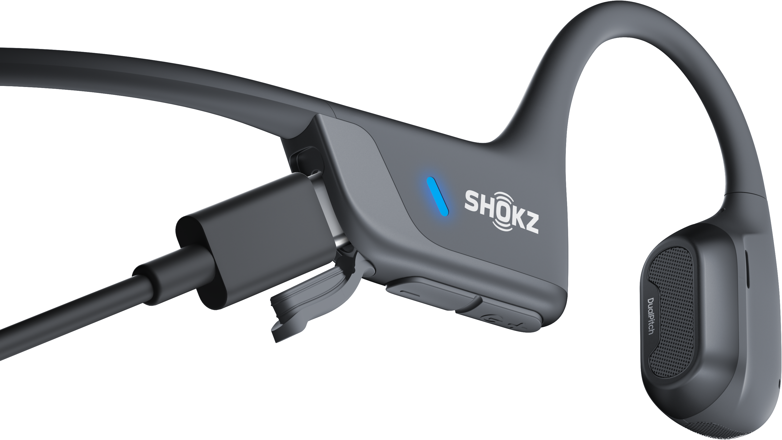Grauer Shokz-Kopfhörer mit eingestecktem Ladekabel. Schwarzer Hintergrund.