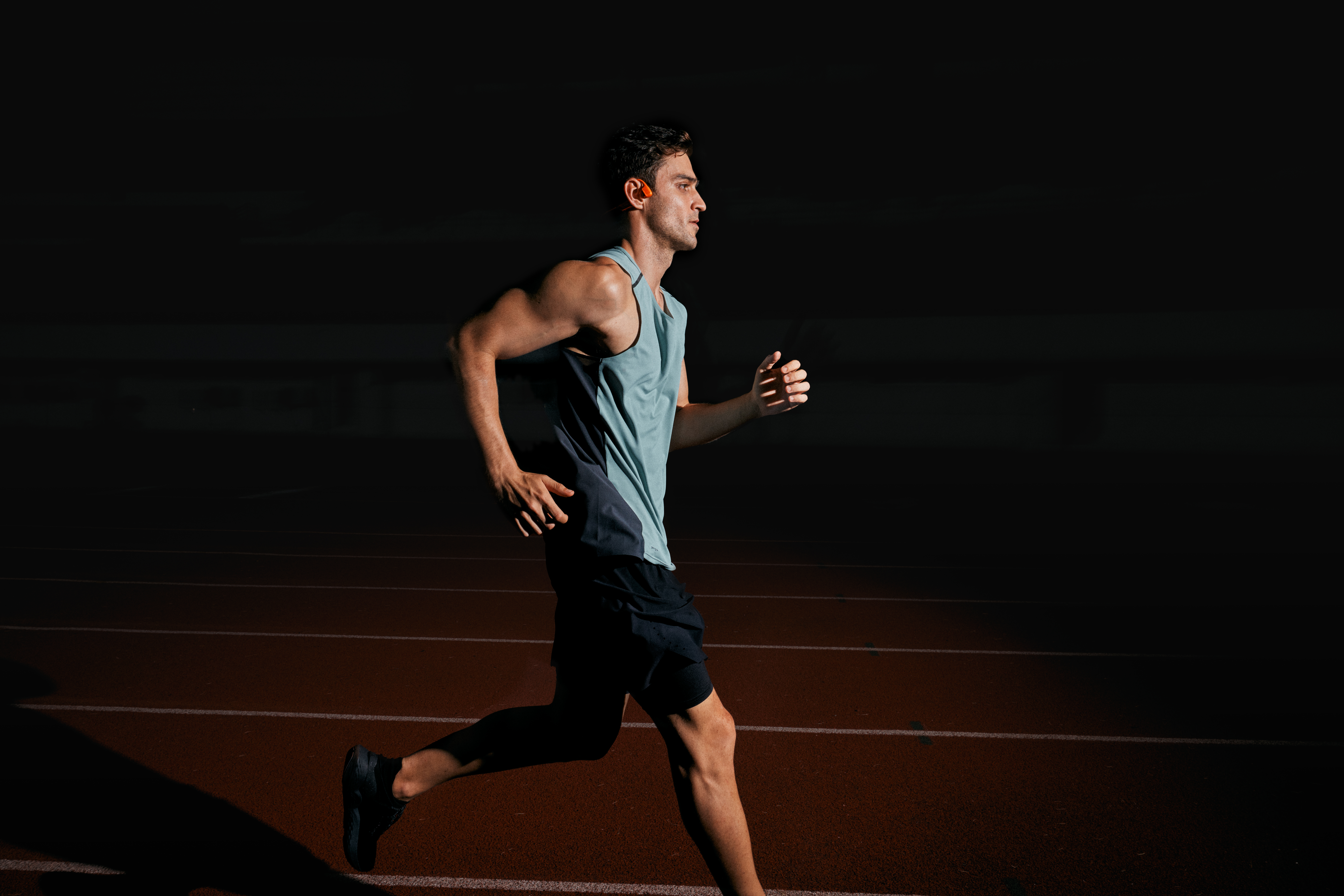 Homme courant sur une piste la nuit, en tenue de sport. Fond noir.