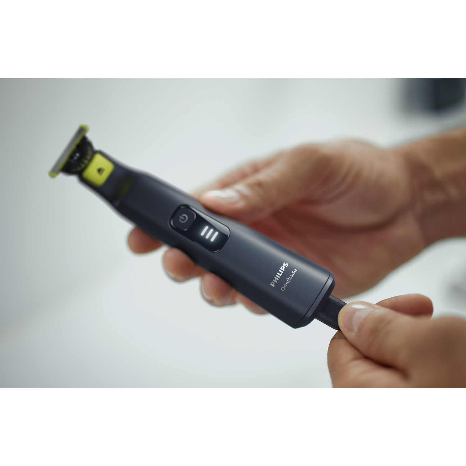 Man die een zwarte en groene Philips OneBlade scheerapparaat vasthoudt. Witte achtergrond.