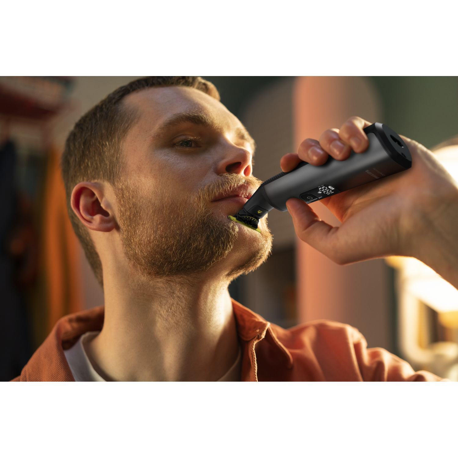 Man shaving his beard with a trimmer. The trimmer is black and the man has a beard.