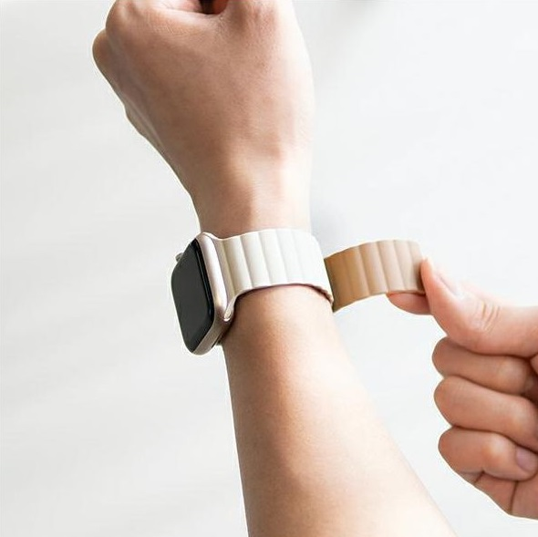 Ręka mocująca beżowy pasek do złotego Apple Watch na nadgarstku.