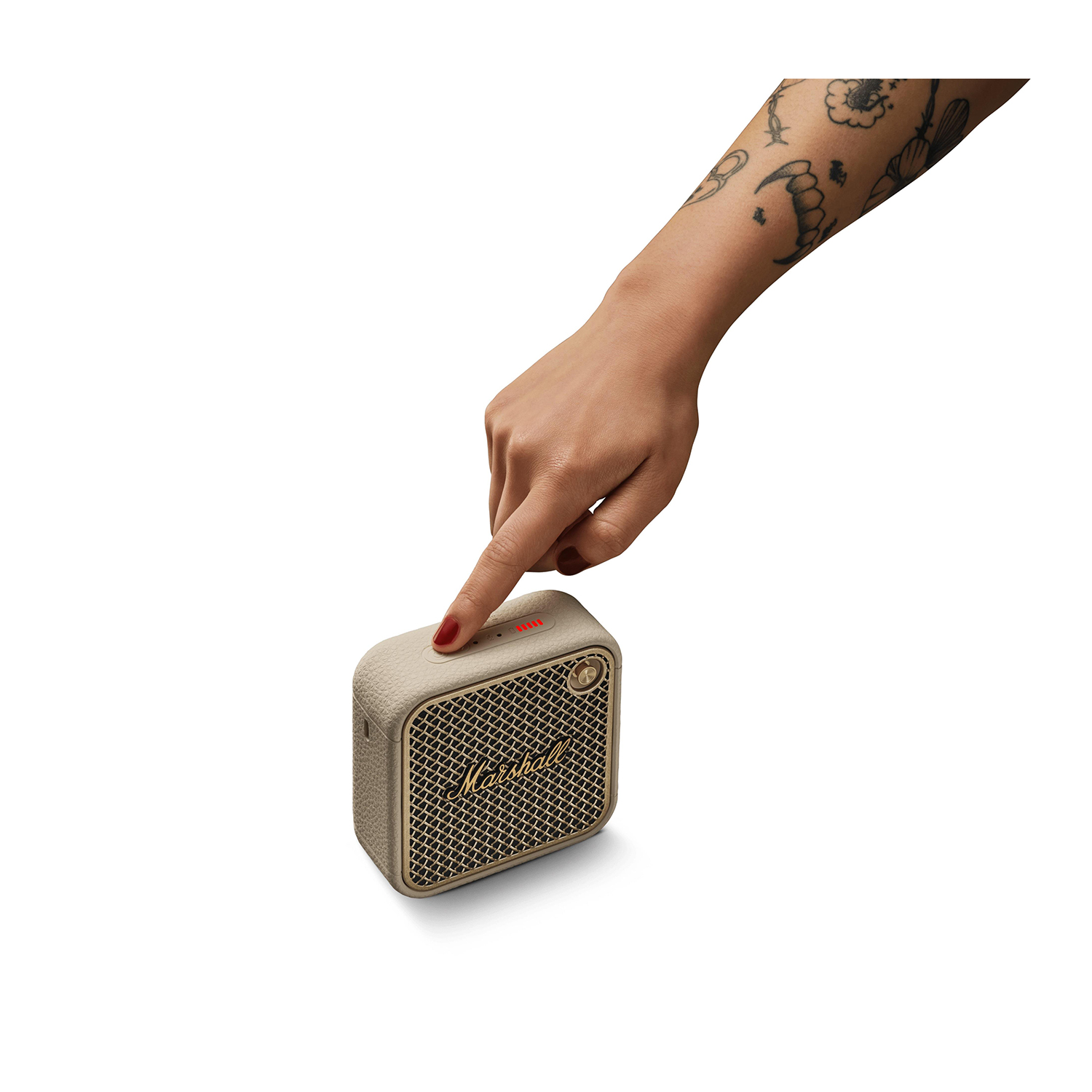 Una mano che preme il pulsante di accensione su un altoparlante Marshall beige, sfondo bianco.